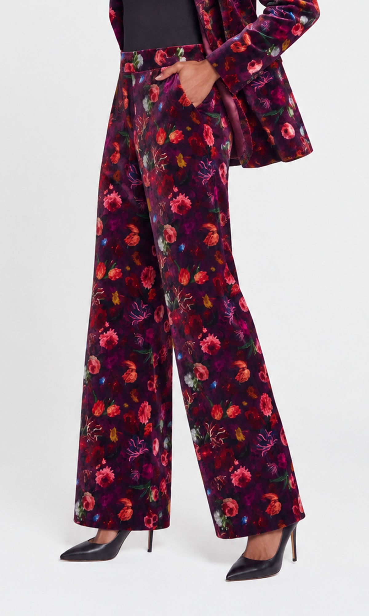 Side view of model wearing high-waisted, wide-leg trousers in a dark purple velvet fabric with a vibrant multicolor floral print, styled with a matching blazer.