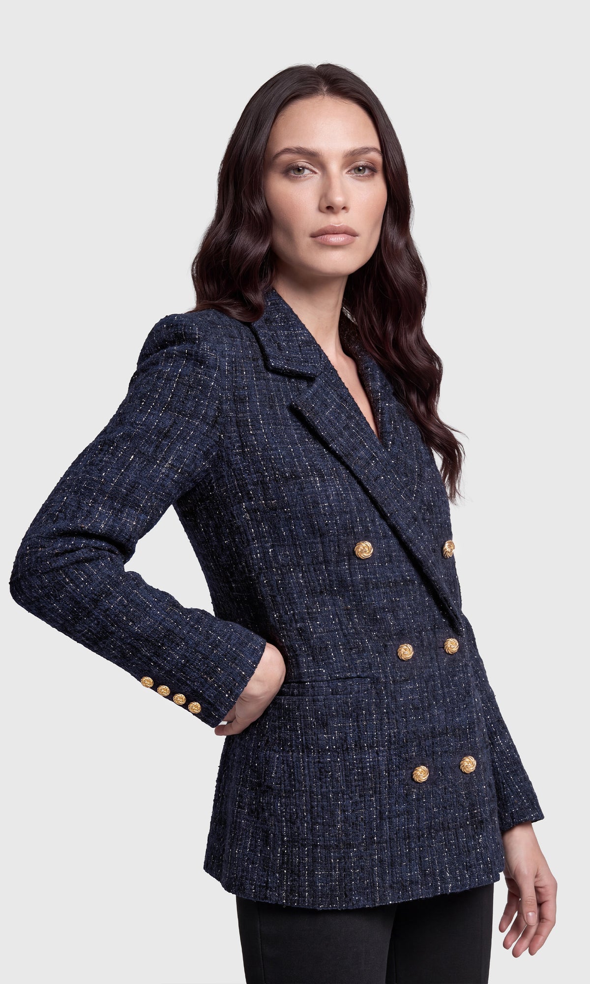 A woman modeling a navy blue double-breasted blazer with a subtle tweed texture and prominent gold buttons.