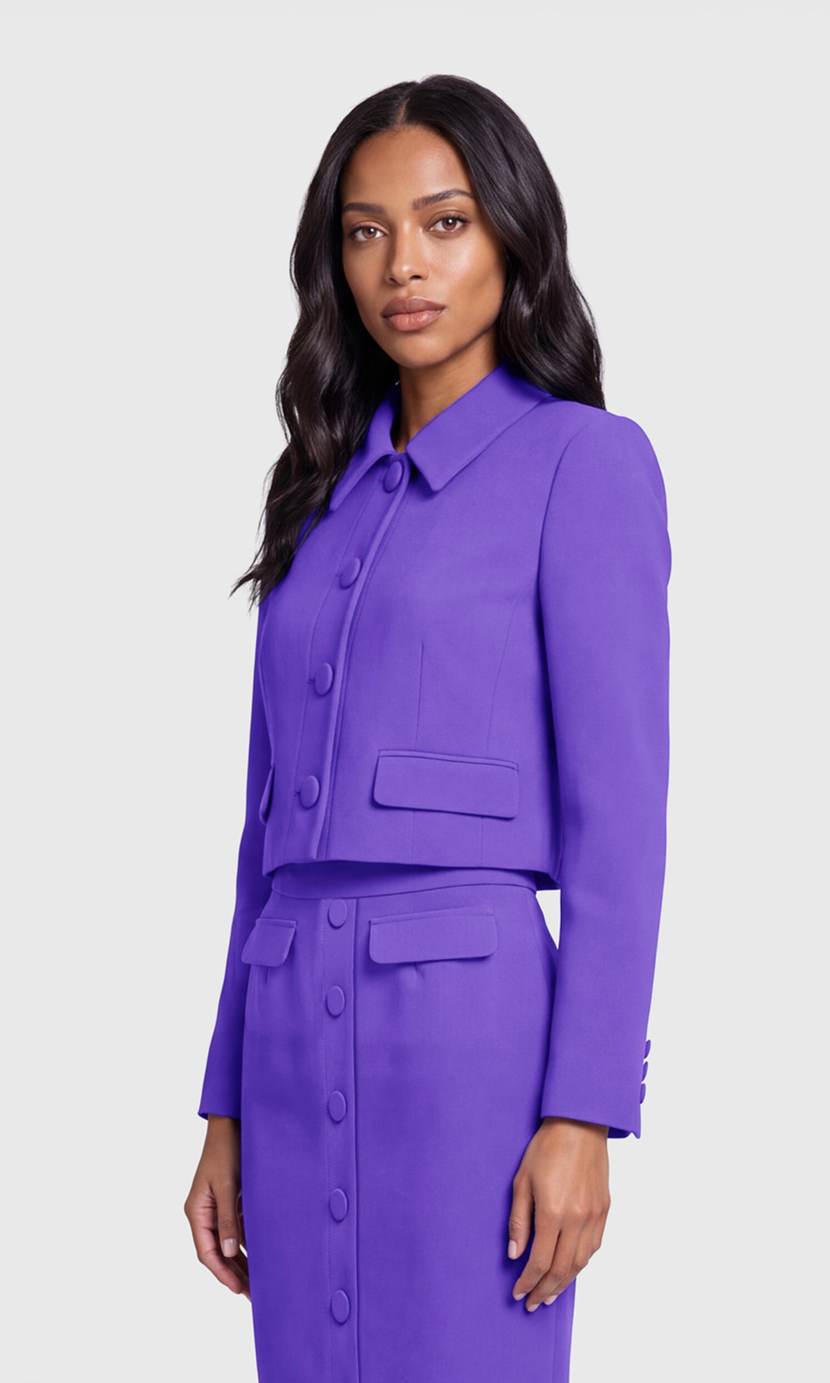 A woman modeling a matching purple long-sleeve button-front jacket and skirt set against a light gray studio background.