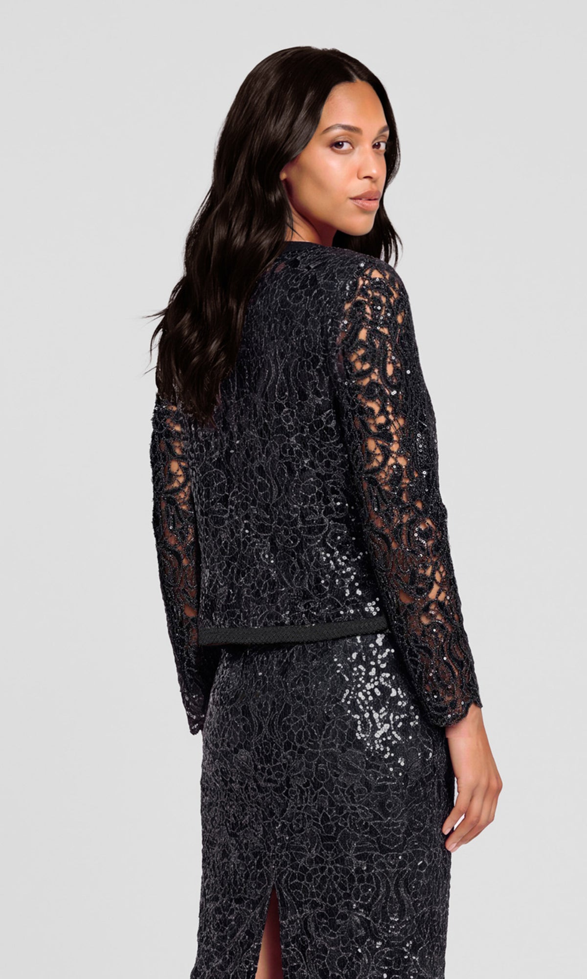 Back view of model wearing a black lace and sequin long-sleeve dress from the back, showing the detailed texture of the lace and sequins.