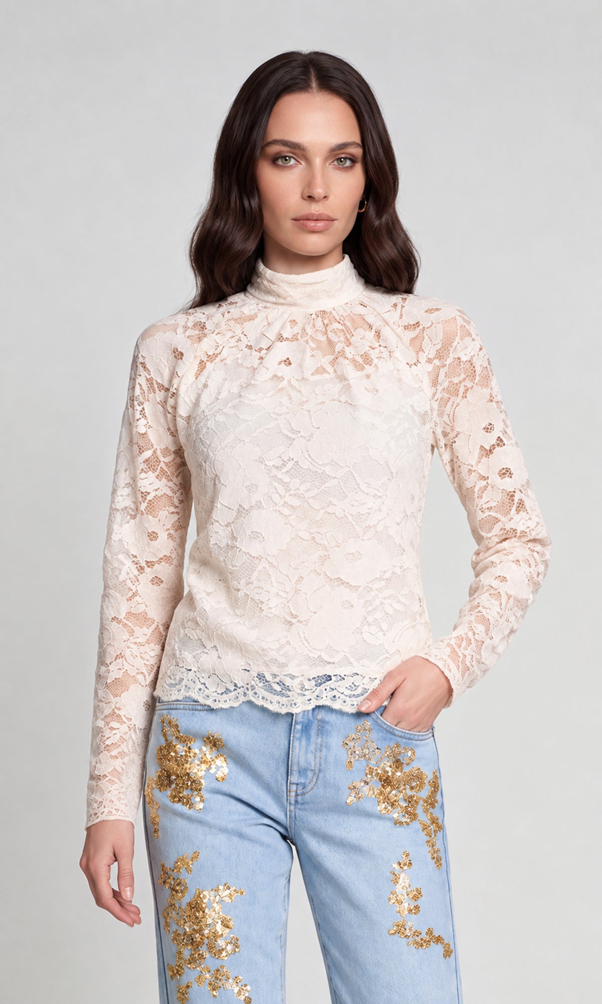 Model wearing a cream lace mock-neck long-sleeve top paired with light blue jeans featuring gold sequin floral embroidery.