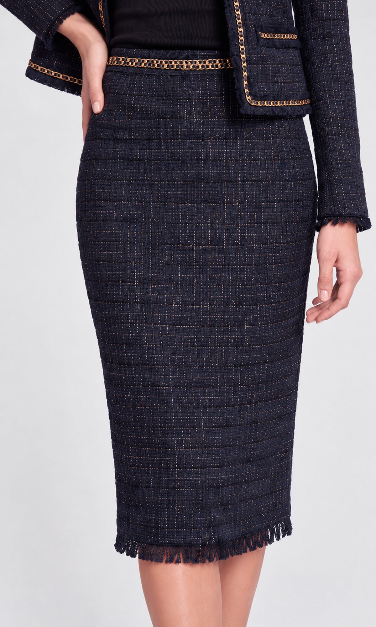 A dark navy blue tweed skirt with gold chain trim at the waistband and hem, paired with a matching blazer.