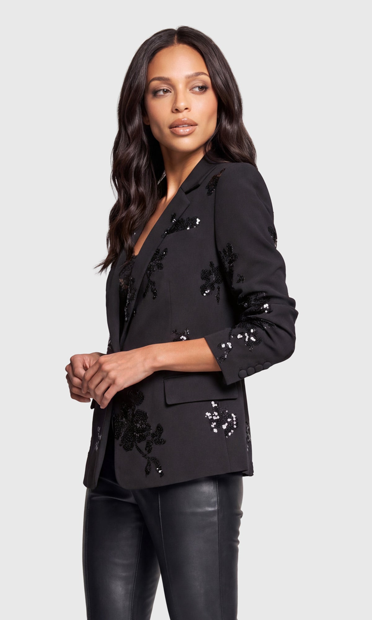 Side view of model wearing a black blazer with black sequined floral embroidery and sequin accents on the lapels, cuffs, and pockets.