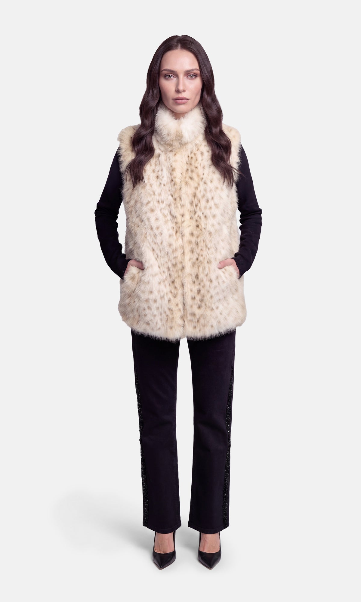 A woman modeling a cream and beige faux fur vest with a subtle leopard print pattern, worn over a black long-sleeve top and black pants.