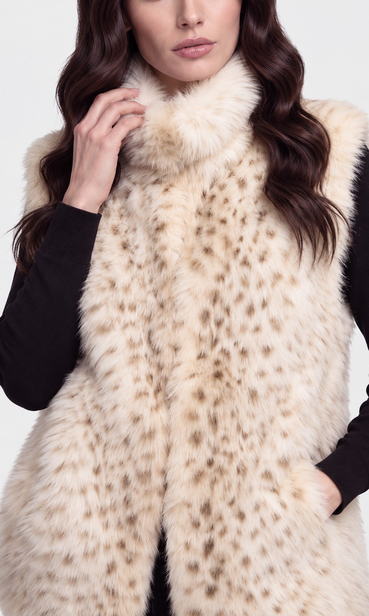 A close-up of a model wearing a sleeveless faux fur vest with a cream and brown spotted pattern and a thick fluffy collar.