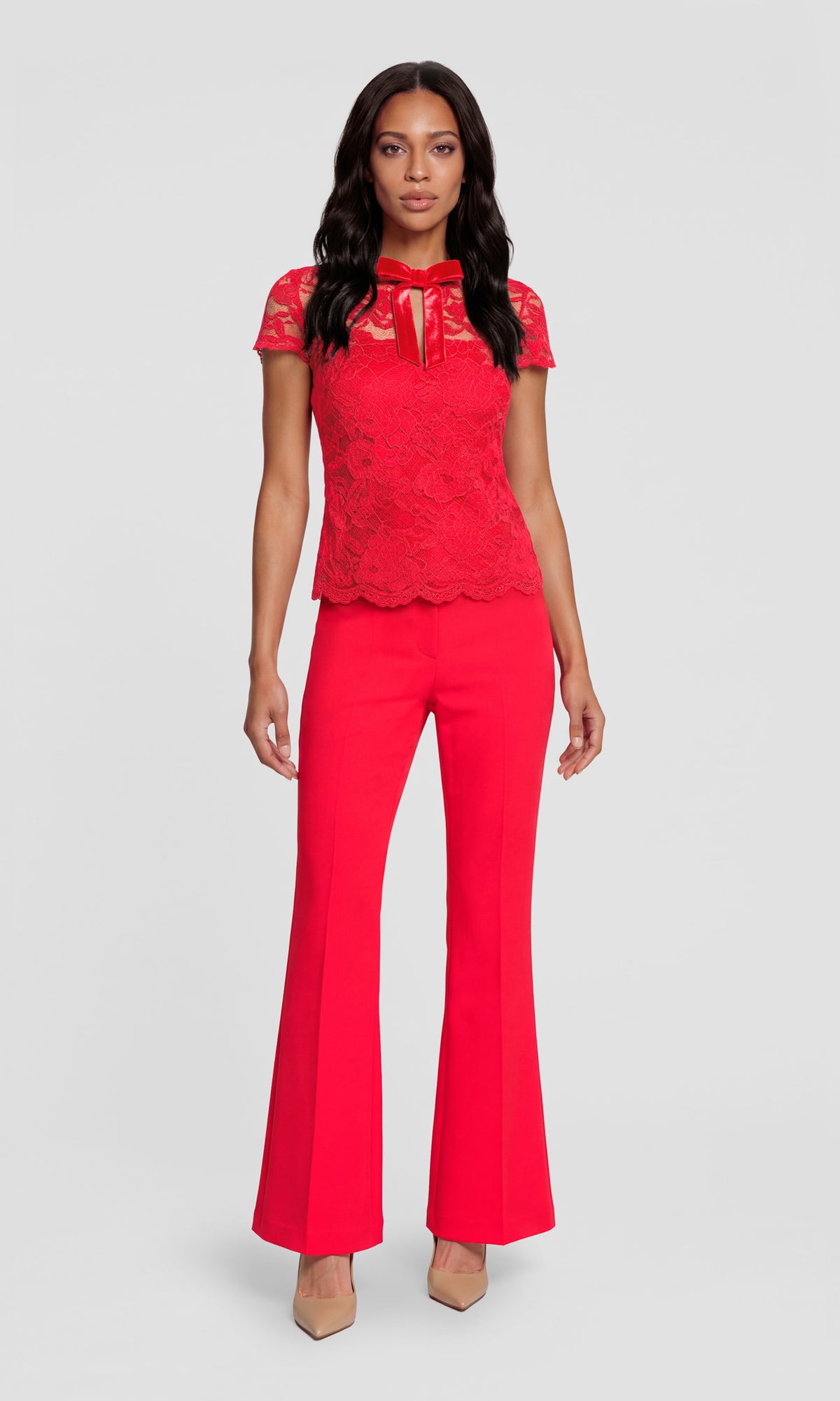 A woman modeling a bright red two-piece outfit consisting of a short-sleeve lace top with a tie neckline and matching red flared pants.