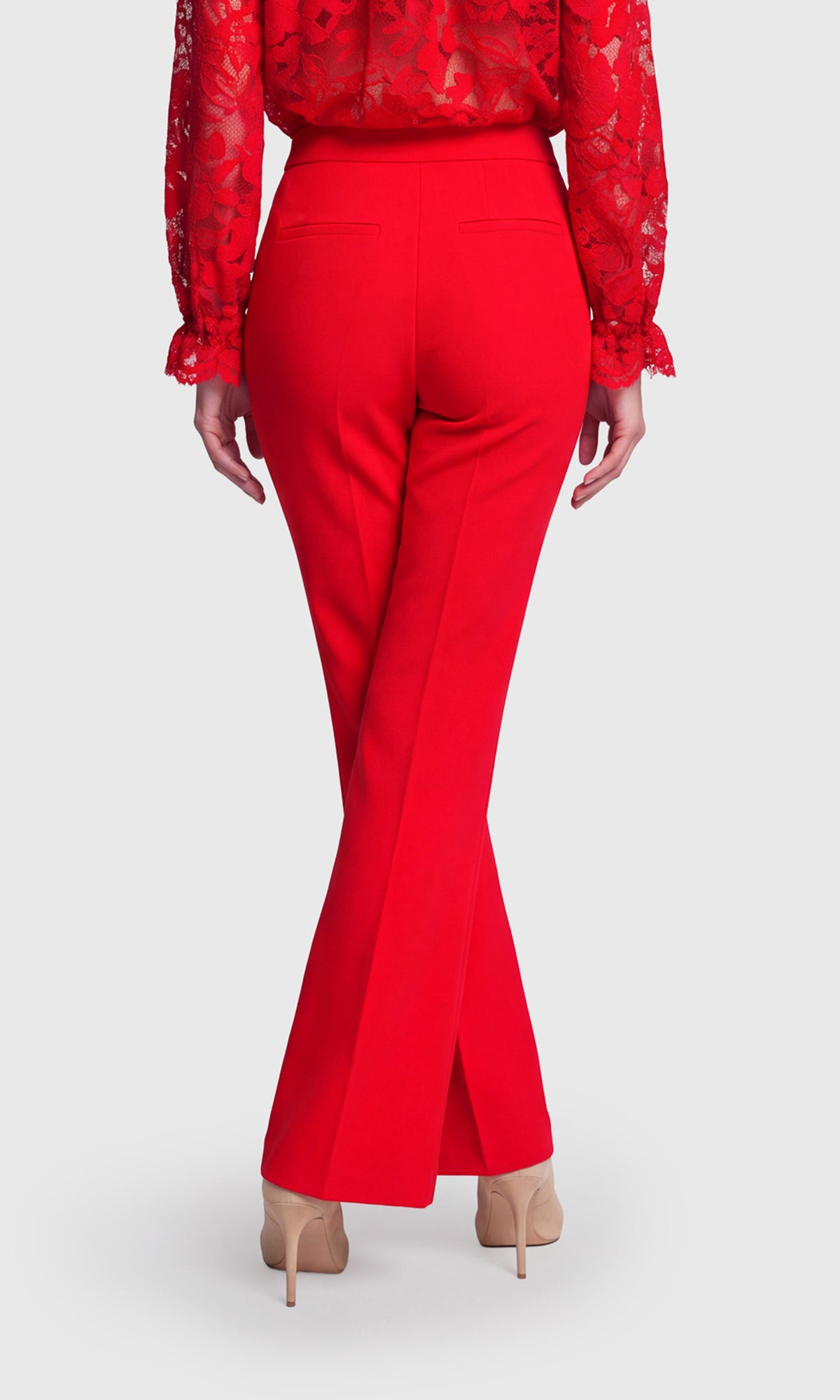 A model shown from the back wearing bright red high-waisted flared trousers and a matching red lace blouse, paired with beige high heels.