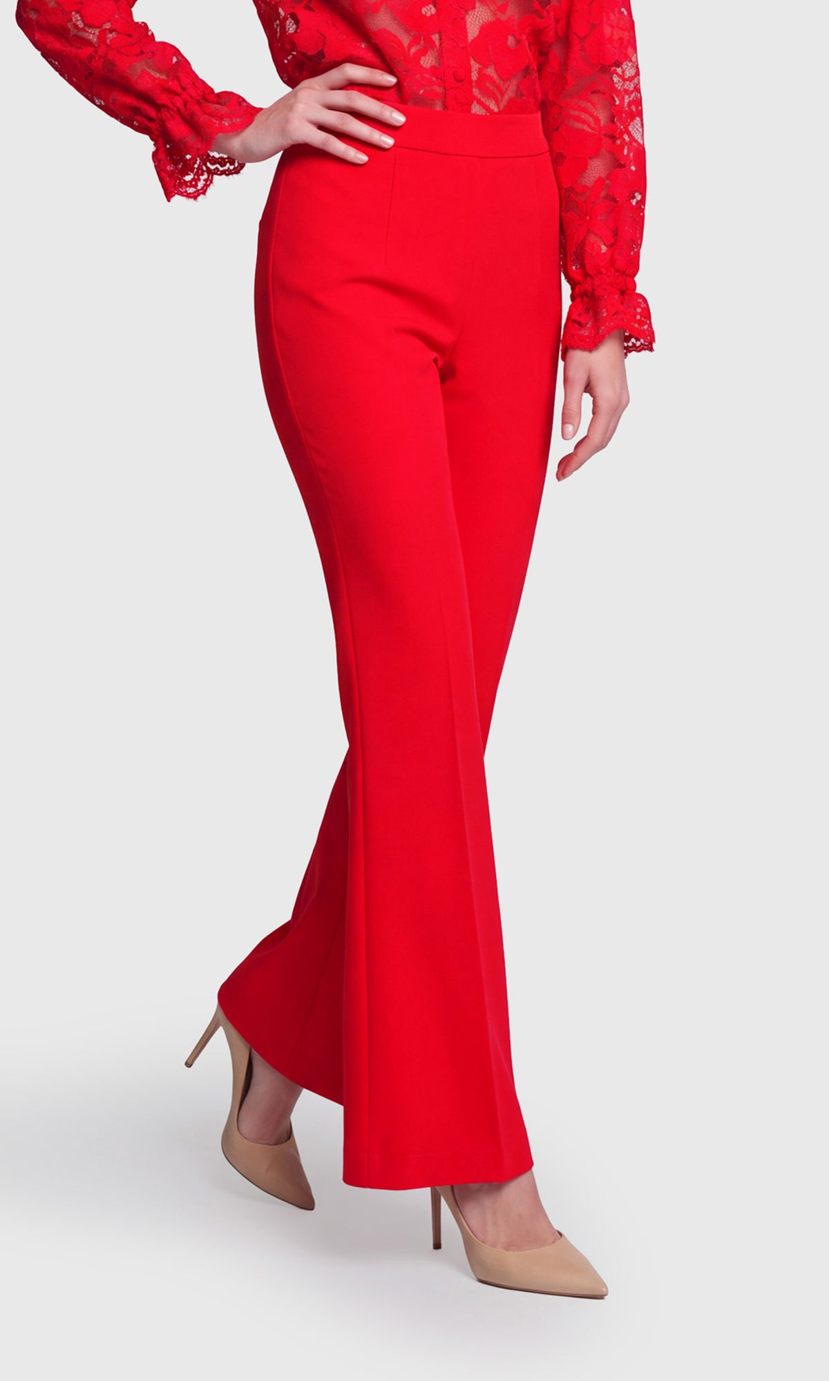 A model wearing bright red high-waisted flared trousers paired with a matching red lace long-sleeve top and beige pointed-toe heels.