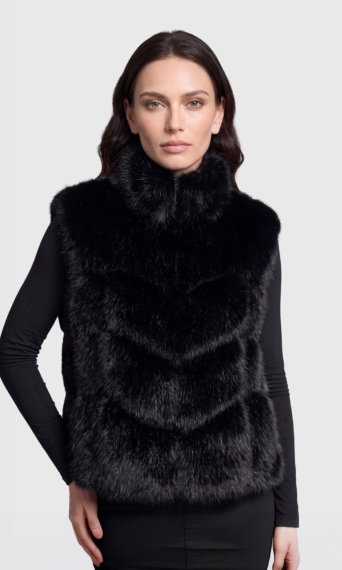 A woman wearing a black fur vest over a black long-sleeve top.