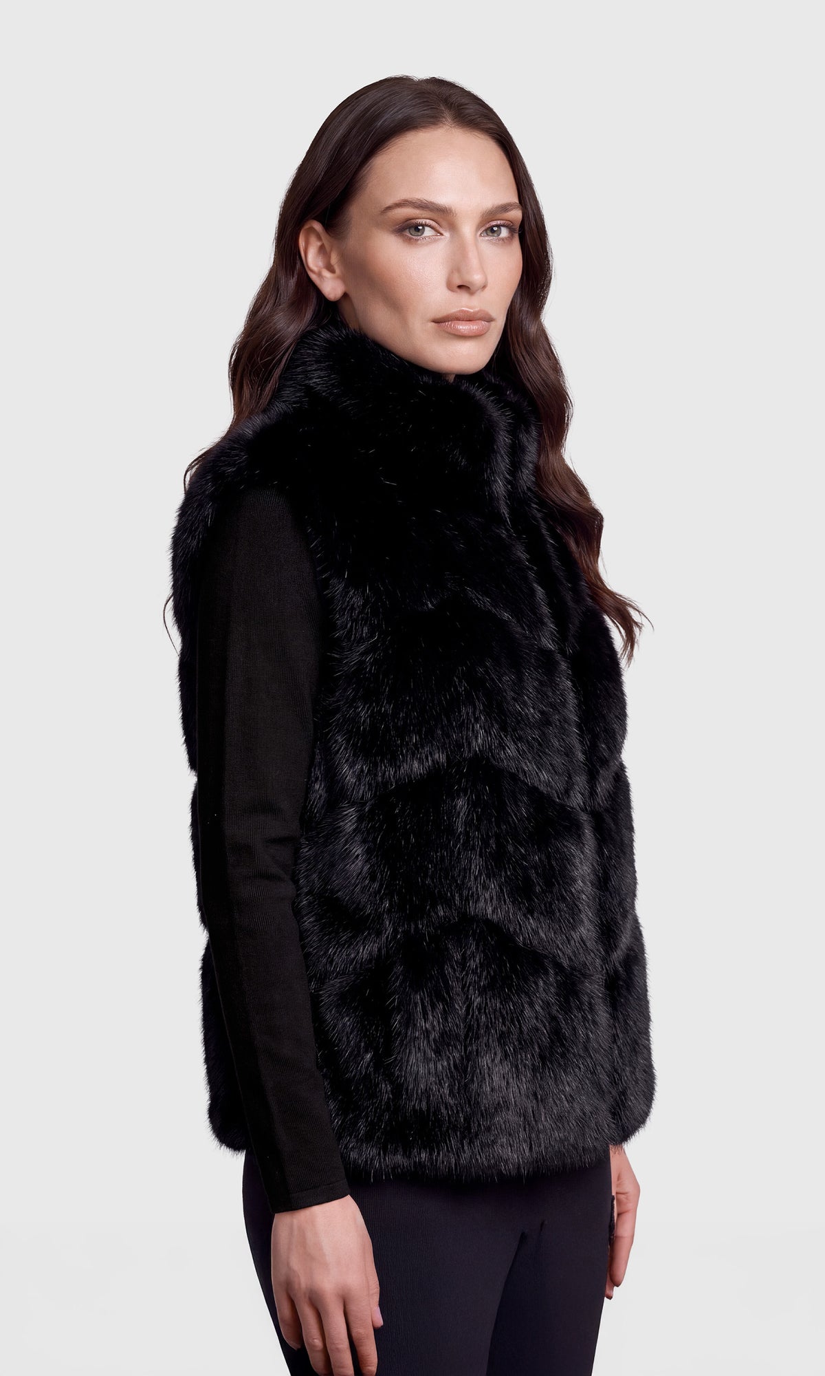 Side view of a woman modeling a black faux fur vest over a black long-sleeve top.