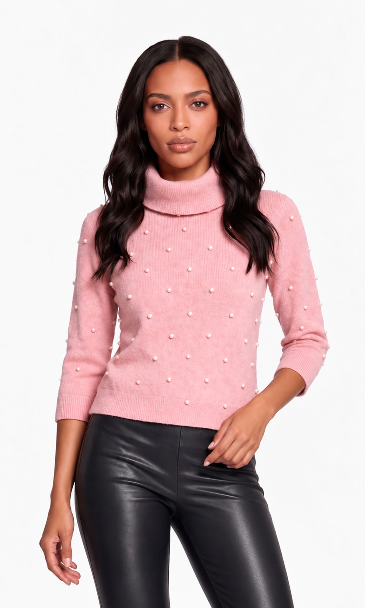 Model wearing a light pink knit turtleneck sweater adorned with small pearl-like embellishments, paired with black faux-leather pants.
