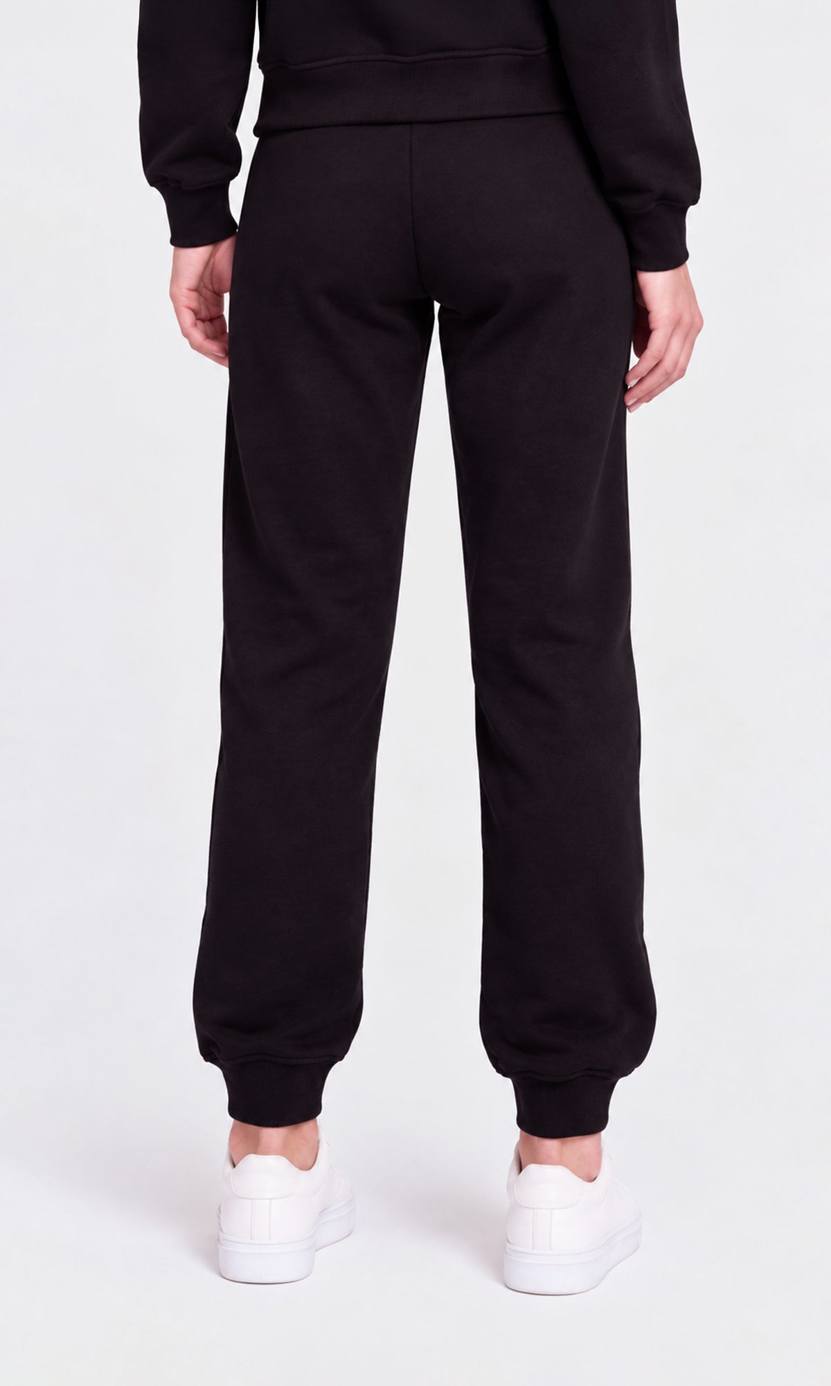 Rear view of a person wearing black sweatpants with elastic cuffs, paired with white sneakers.