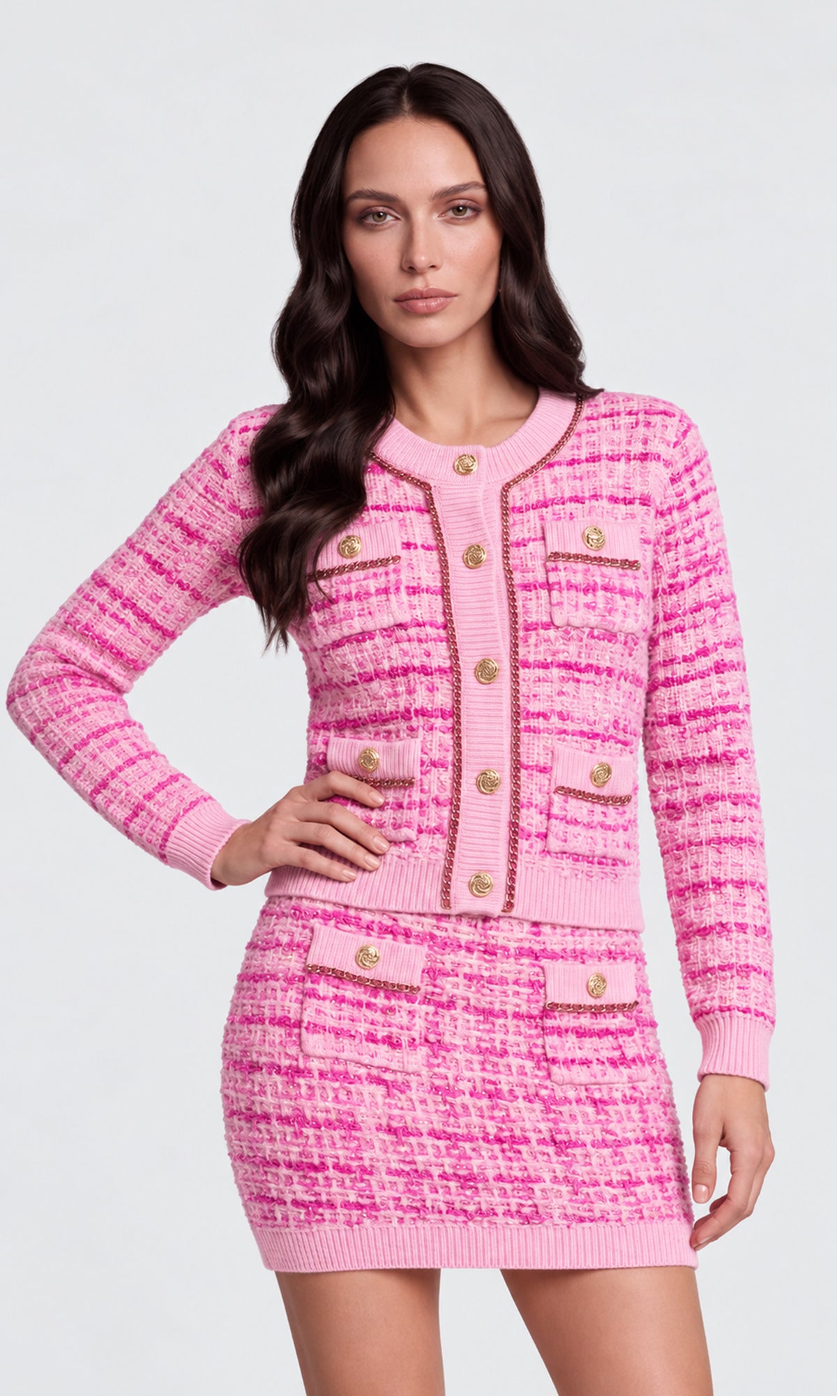 Model wearing a pink tweed cardigan and matching mini skirt set with gold-tone buttons and trim.