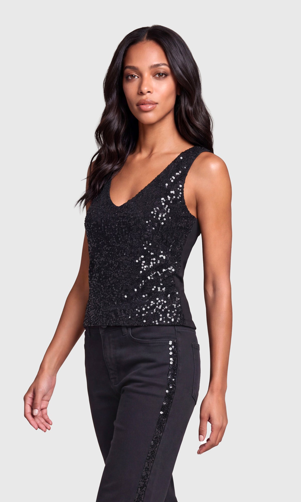 Side view of model wearing a black sequined sleeveless tank top paired with black jeans.