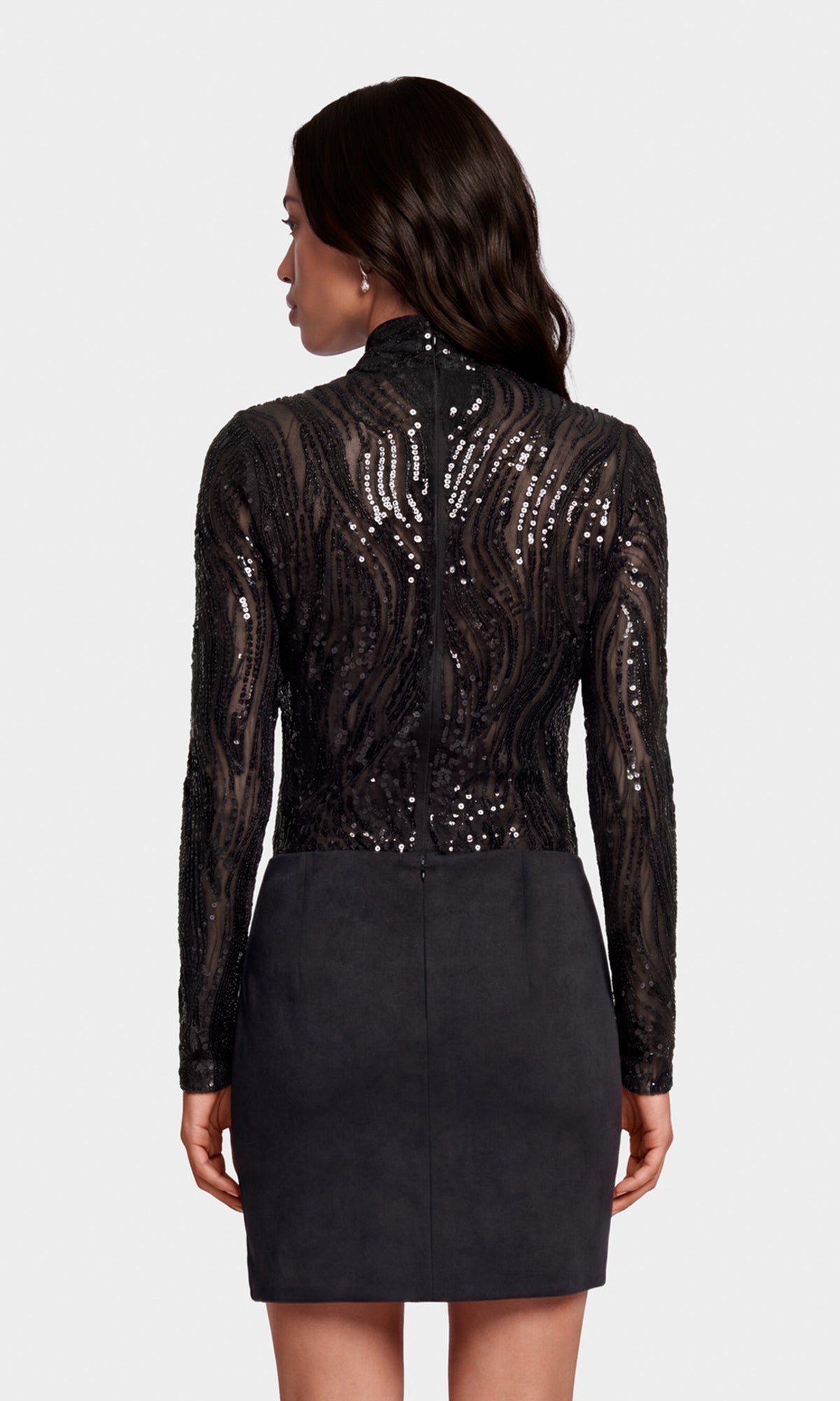 Back view of model wearing a black mock neck mesh and sequins embellished top with a black suede mini skirt.