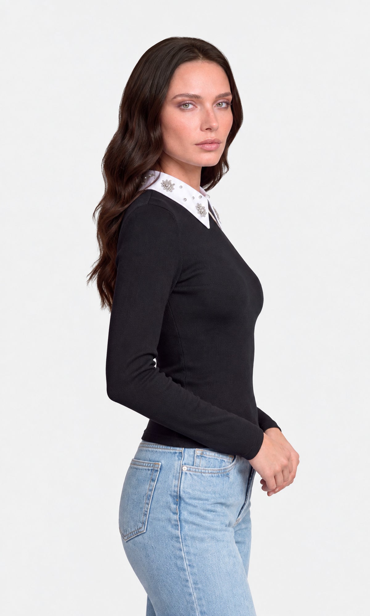 Side view of model wearing a black long-sleeve knit sweater with a contrasting white pointed collar decorated with small silver floral motifs, paired with light blue jeans.