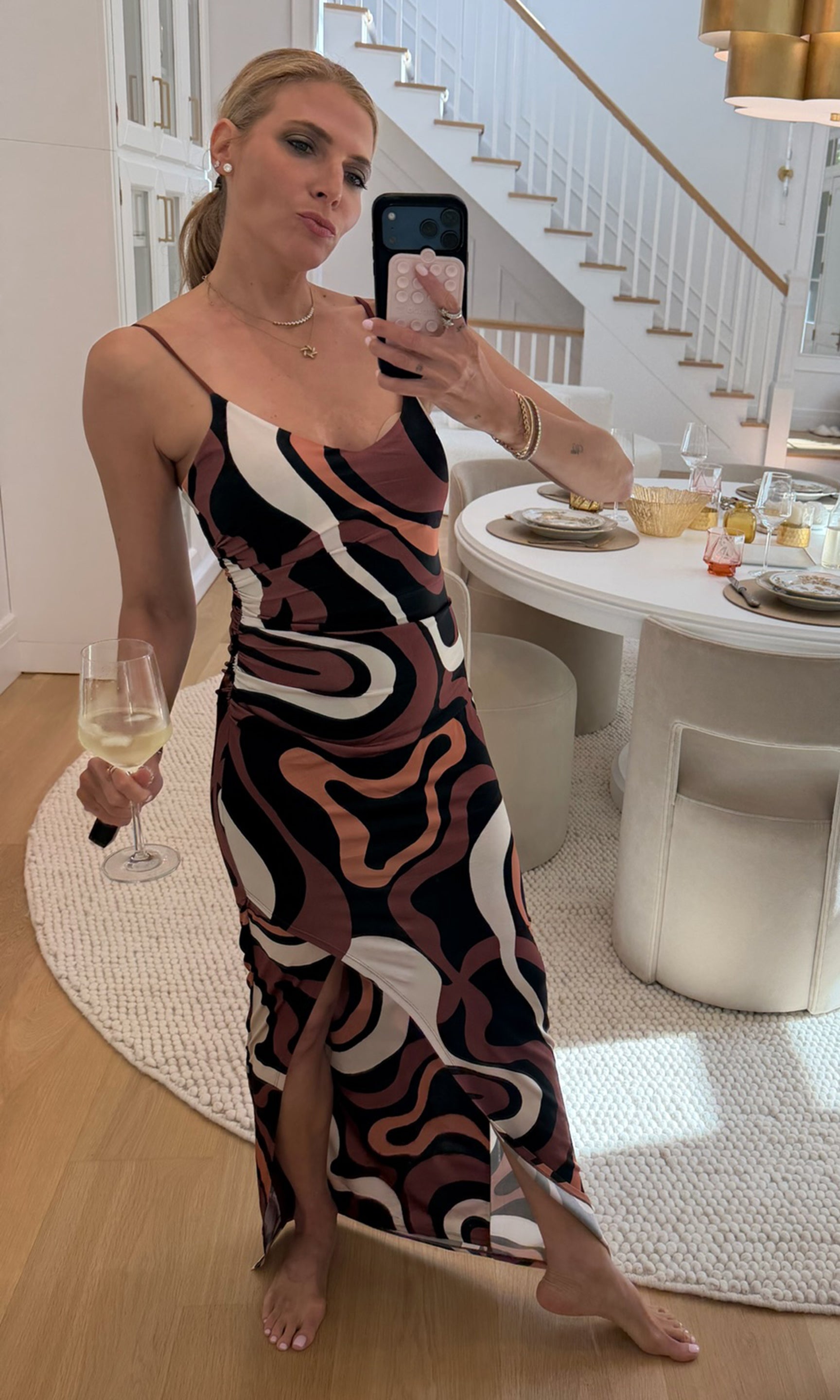 Our founder takes a mirror selfie wearing a sleeveless spaghetti-strap maxi dress with a brown, beige, and black wavy abstract pattern.