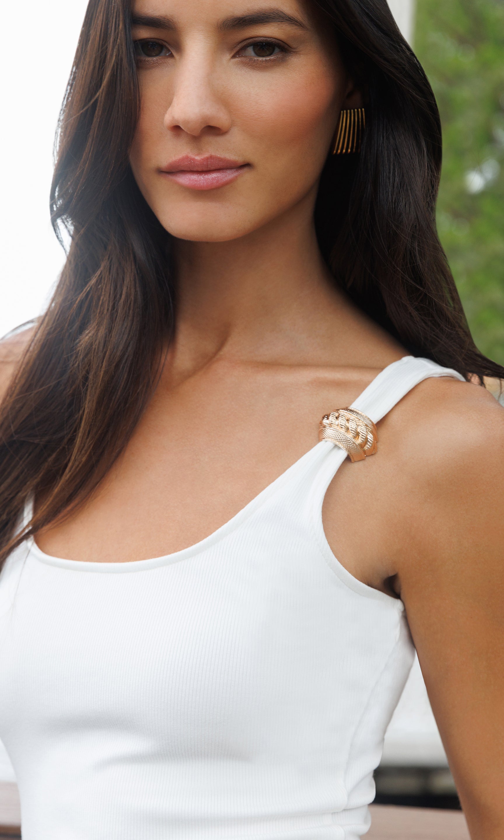 Woman wearing a white top with a gold accent on the shoulder outdoors