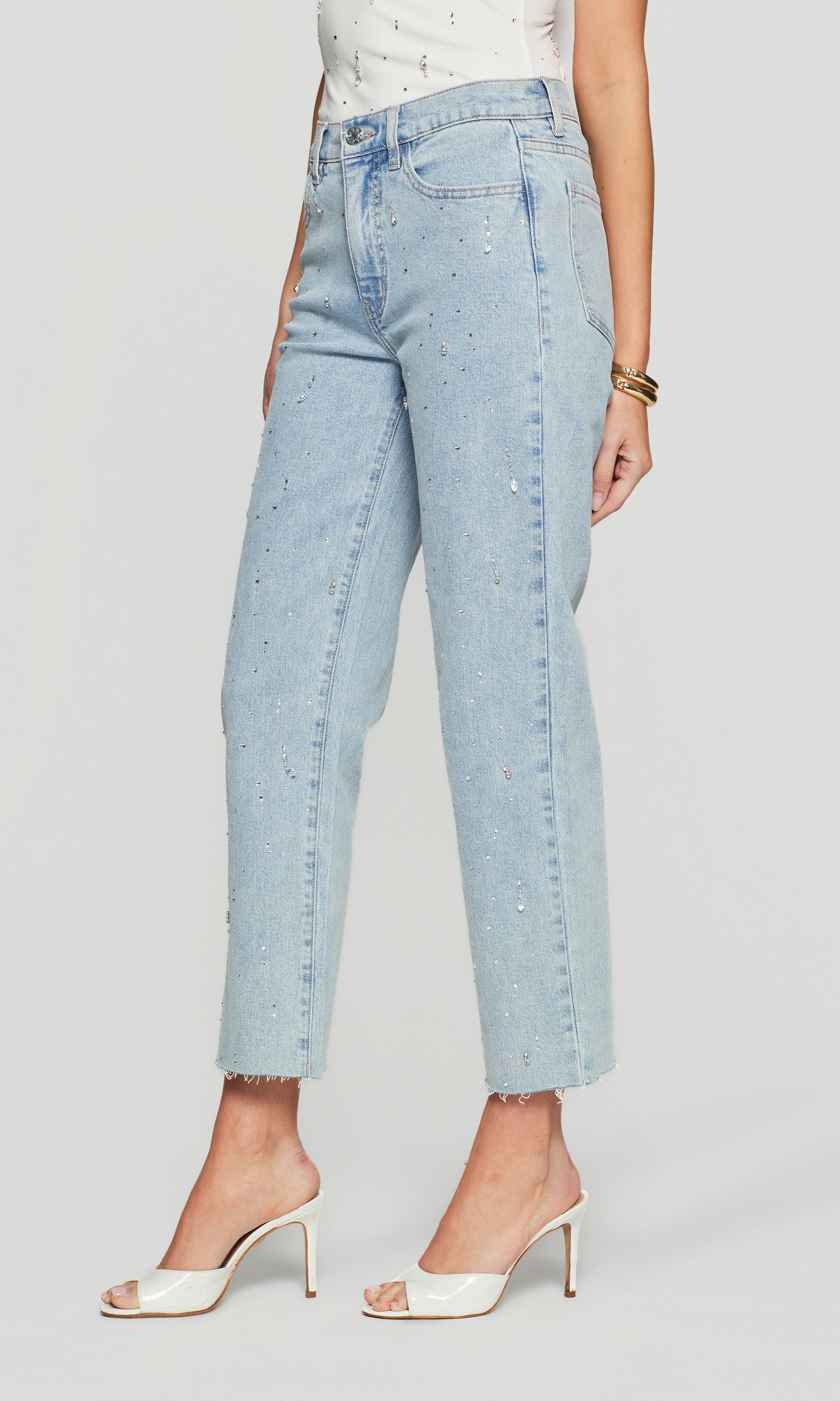Side view of light blue jeans with crystal accents worn by a person on a plain background
