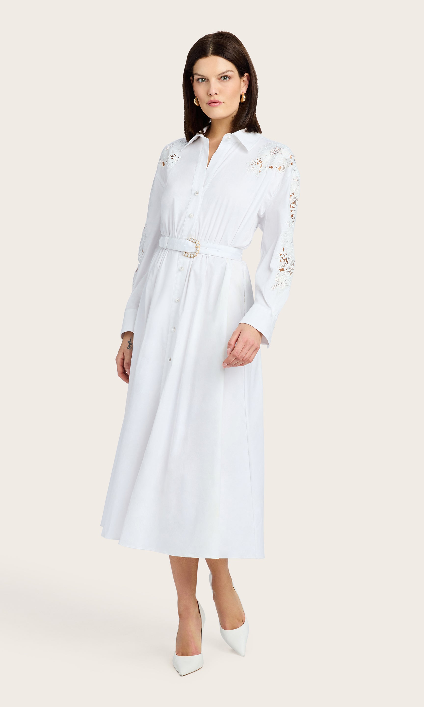 3/4 front view of the model wearing a white button-down lace combo dress with a belted waist and long sleeves, styled with white heels