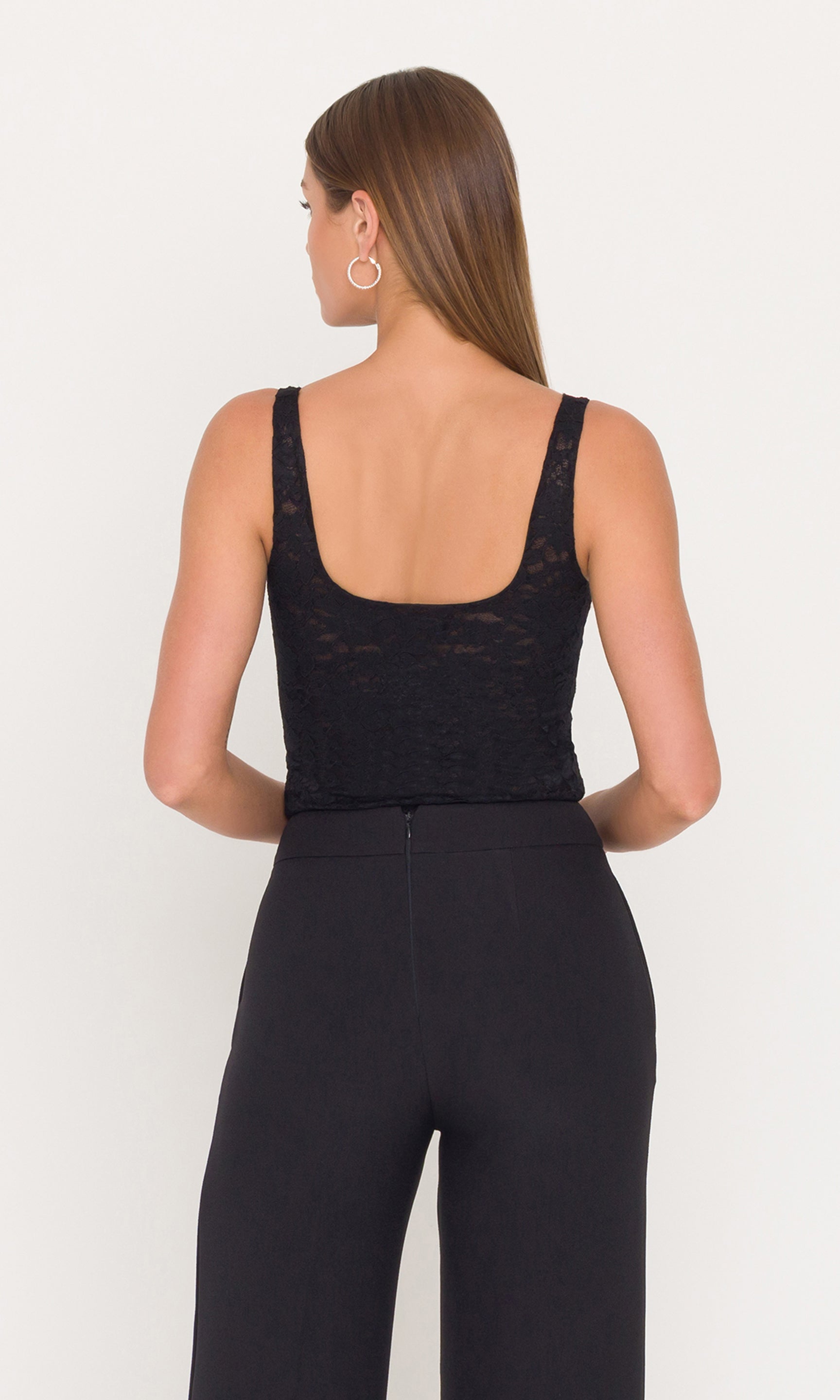 Back view of woman wearing a black lace tank and black pants on a white background