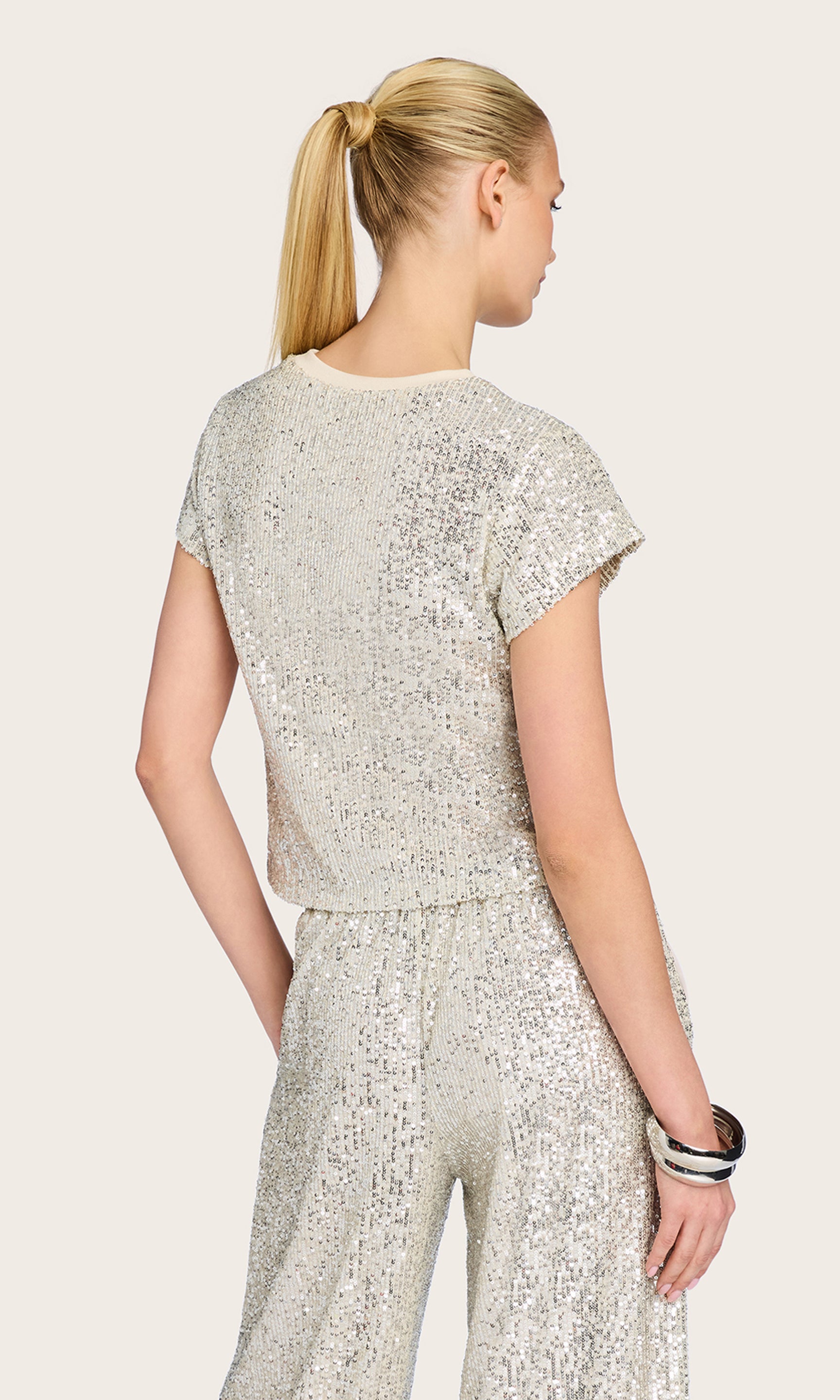Rear view of the model in the Kai Sequin Top in silver, showcasing the clean back silhouette and short sleeve detail.