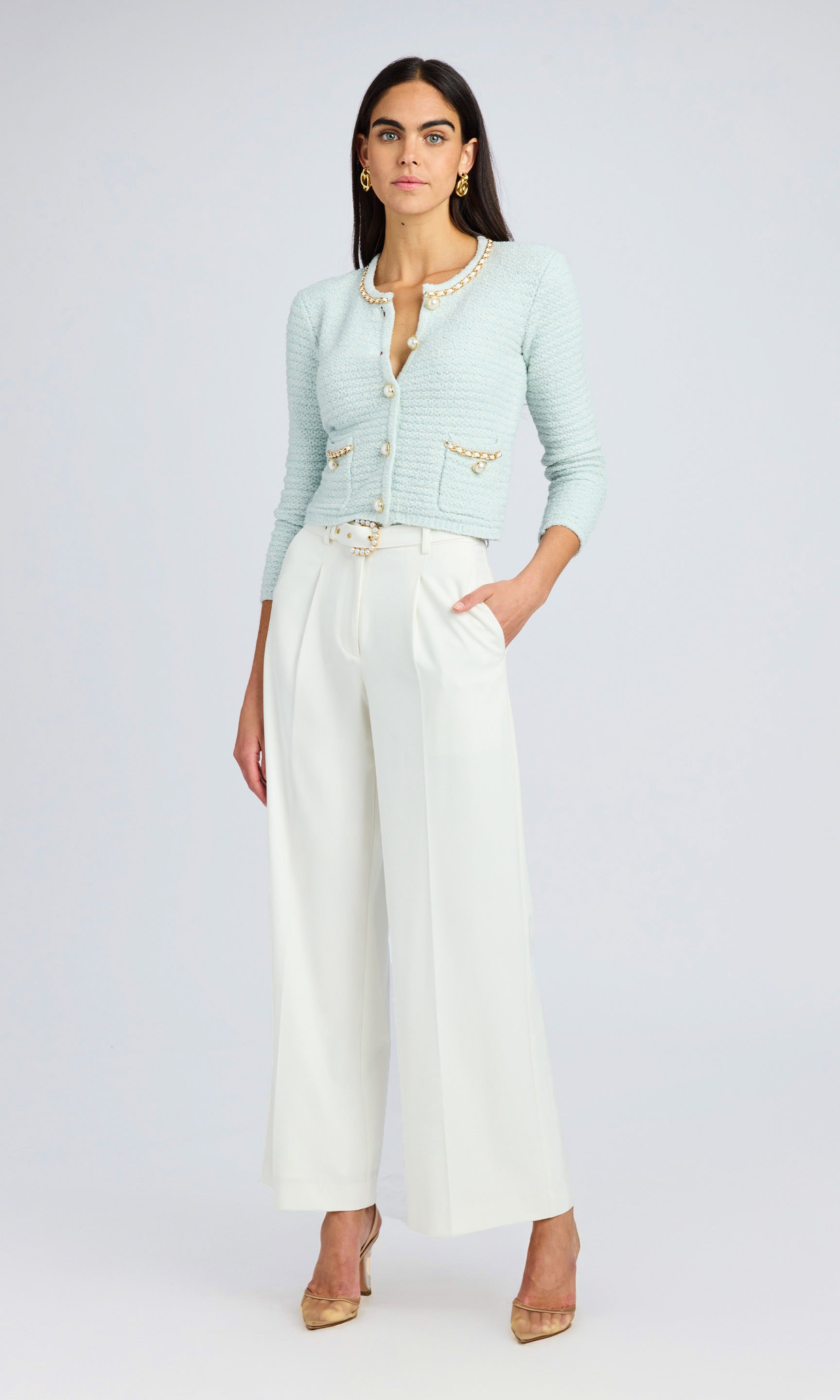model wearing opal colored cardigan sweater with white crepe pant. Both top and bottoms feature gold hard wear and faux pearls.