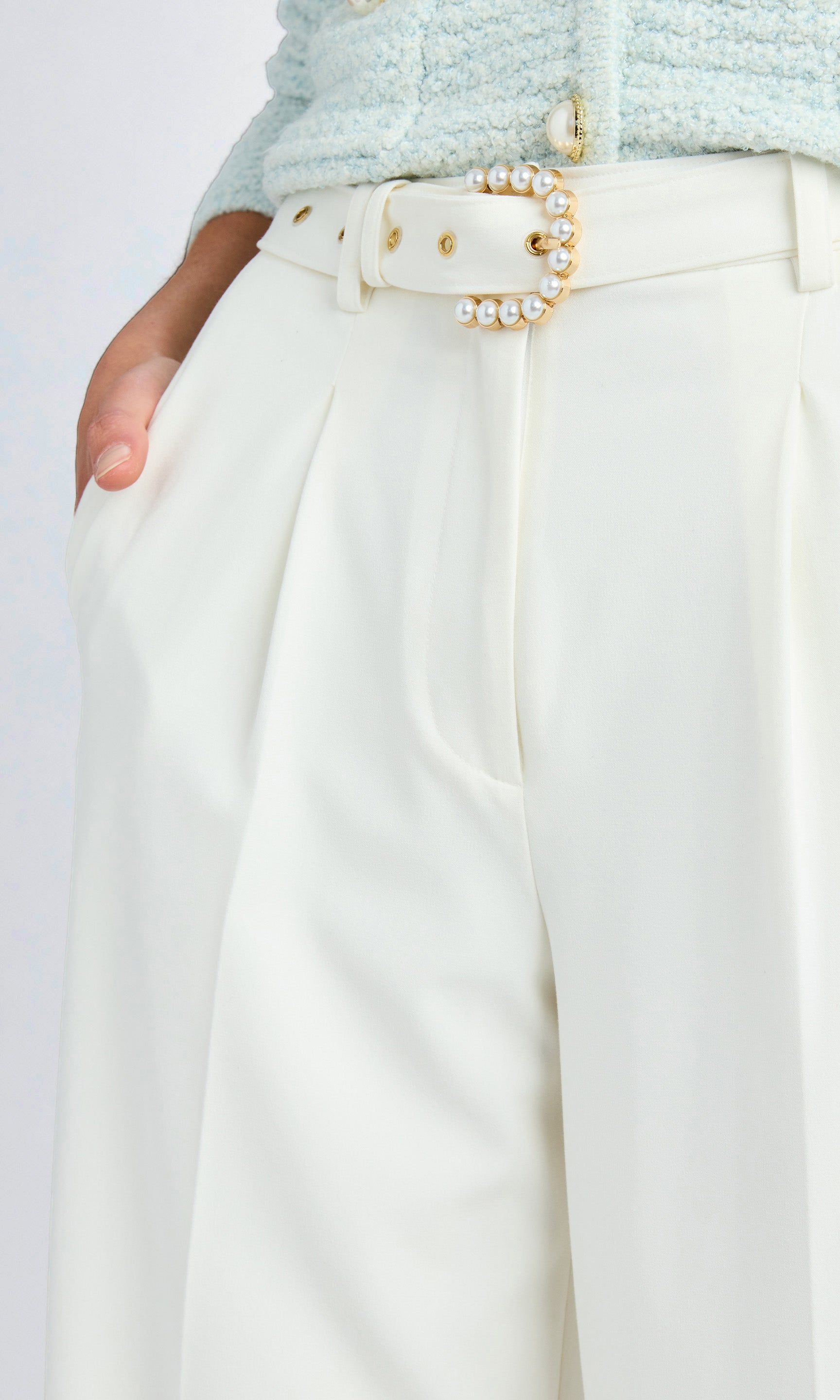 Close up of white crepe pants with faux pearl belt buckle.