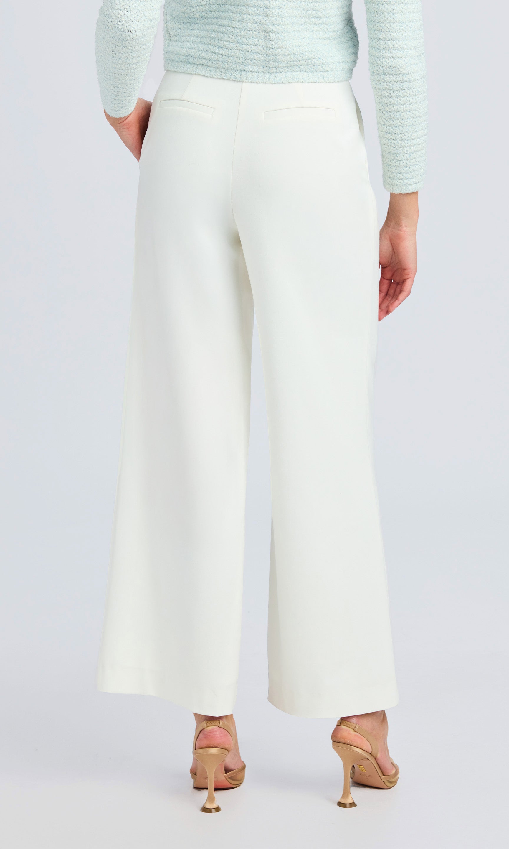 back view of model wearing white crepe pants gold high heels.