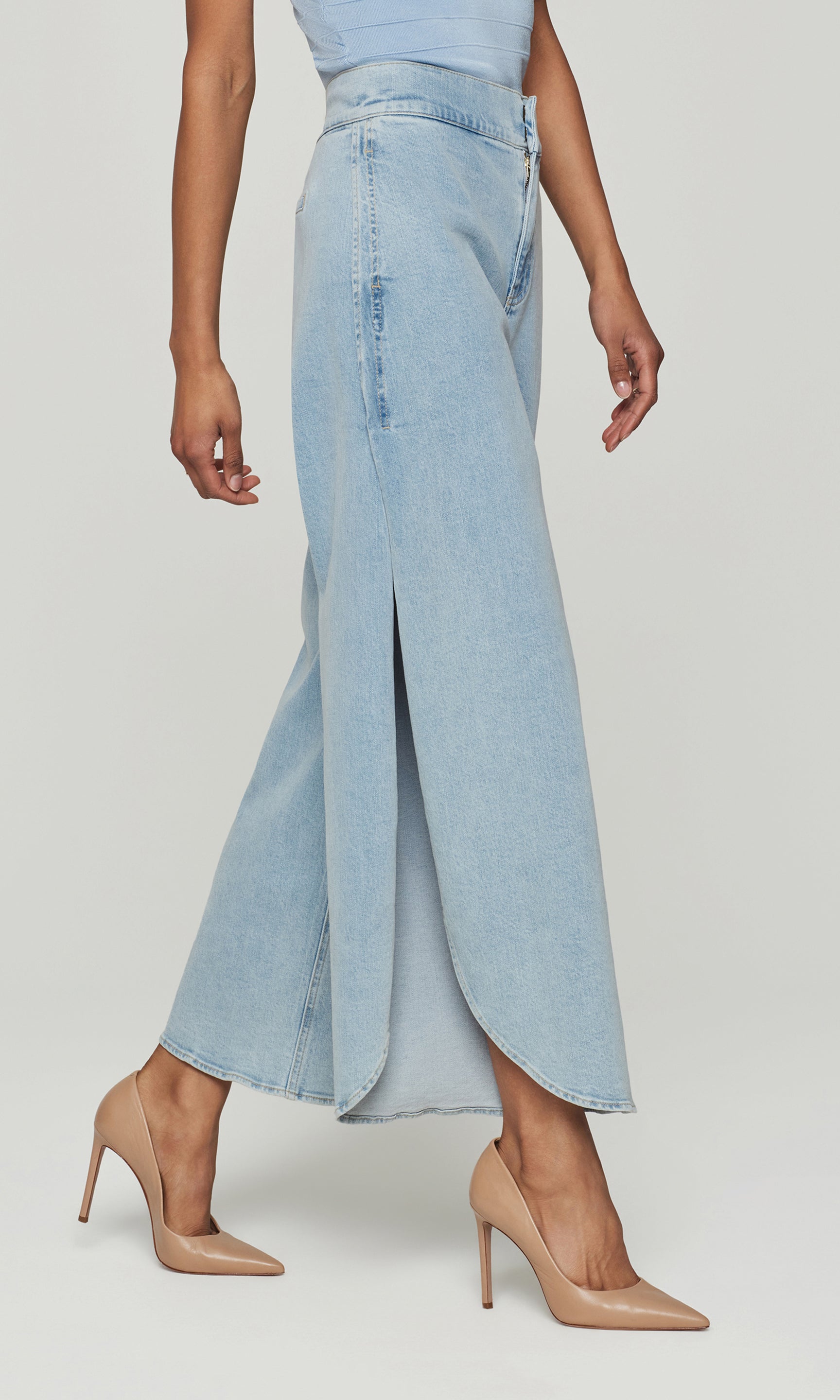 Side view of light blue denim jeans with a side slit worn by a person on a white background