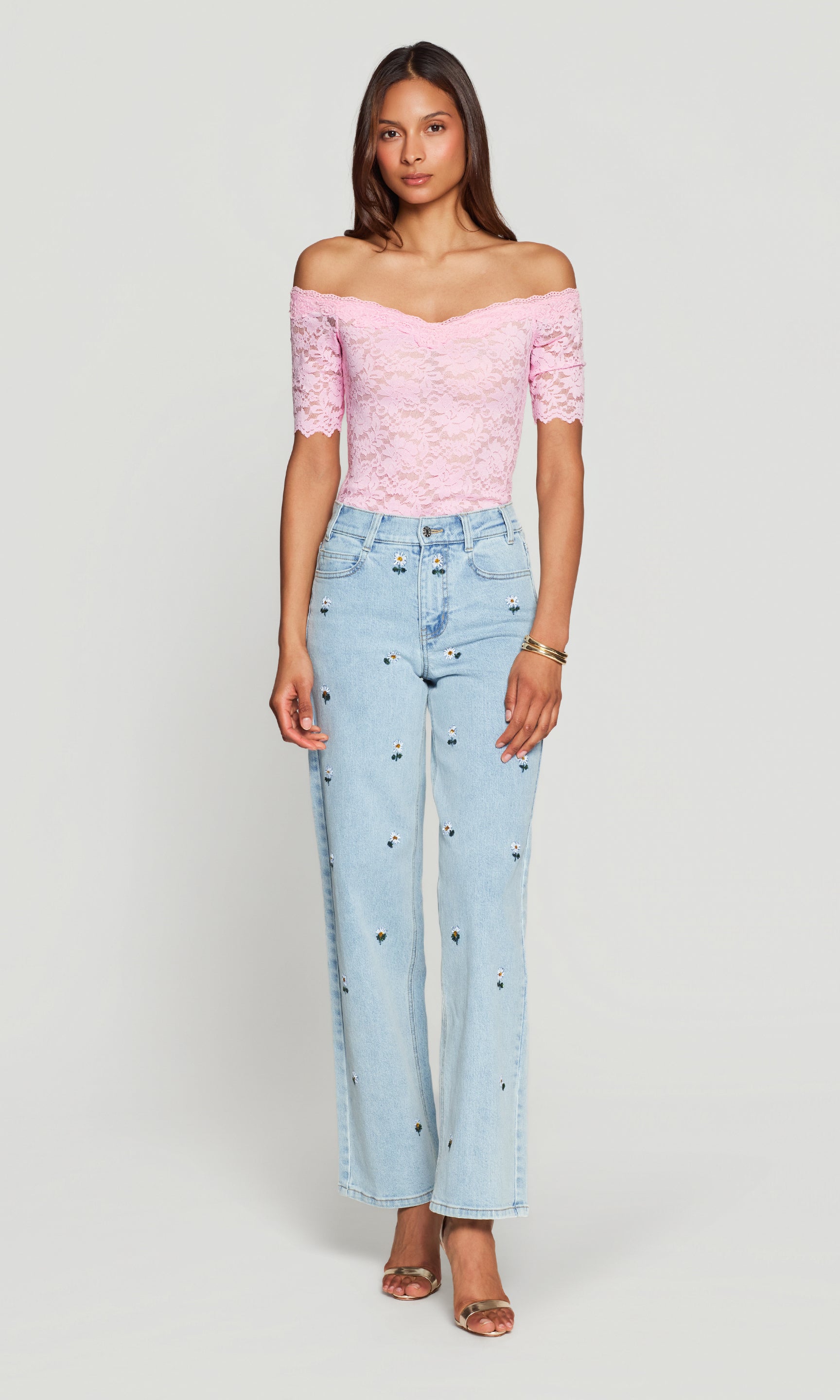 Woman wearing a pink off-shoulder top and light blue jeans on a white background