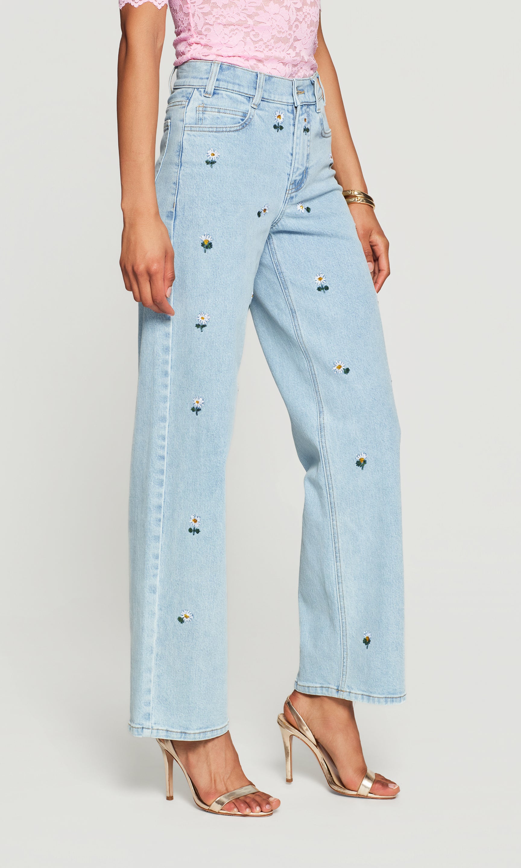 Side view of light blue jeans with decorative daisies worn by a person on a light gray background