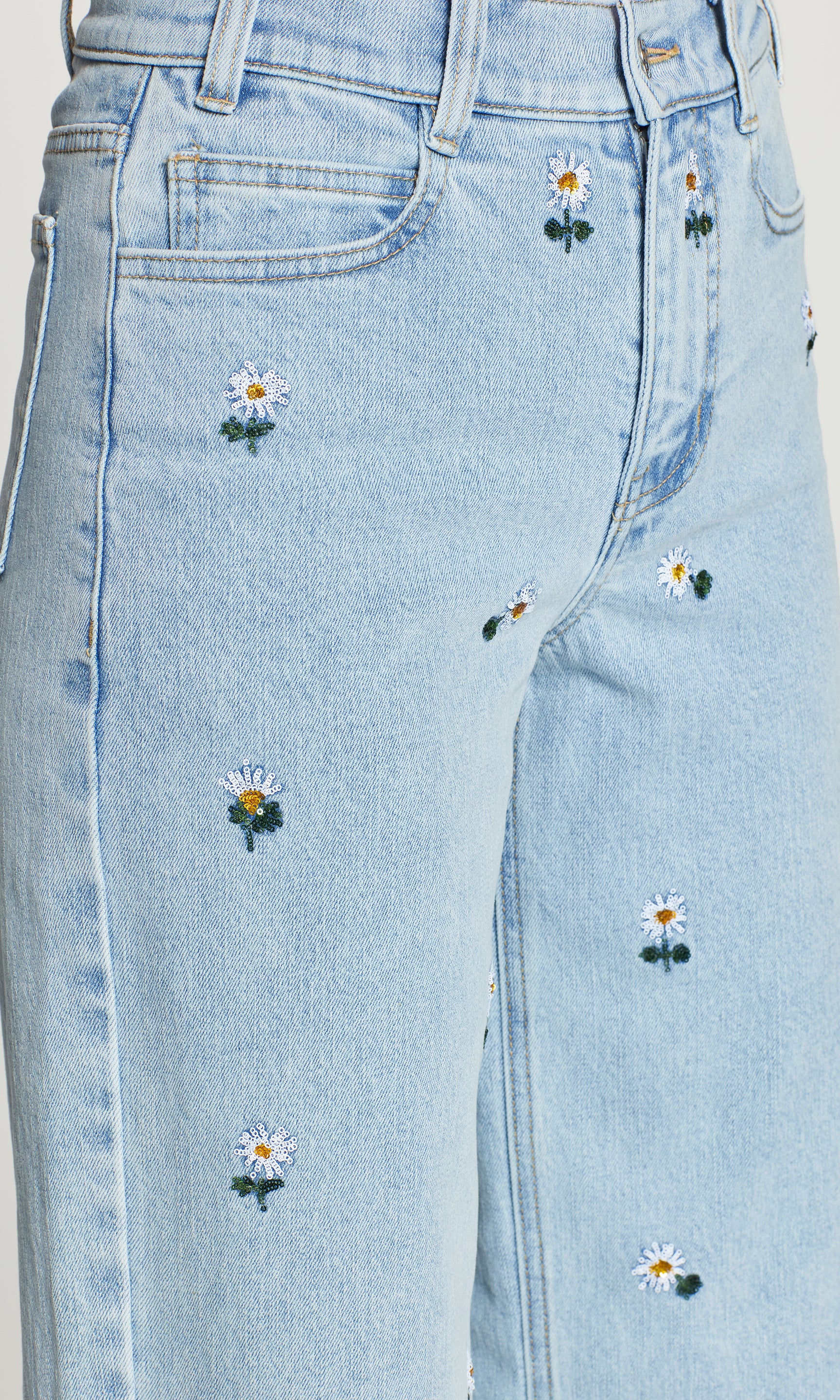 Close-up of light blue jeans with embroidered daisy flowers on a plain background