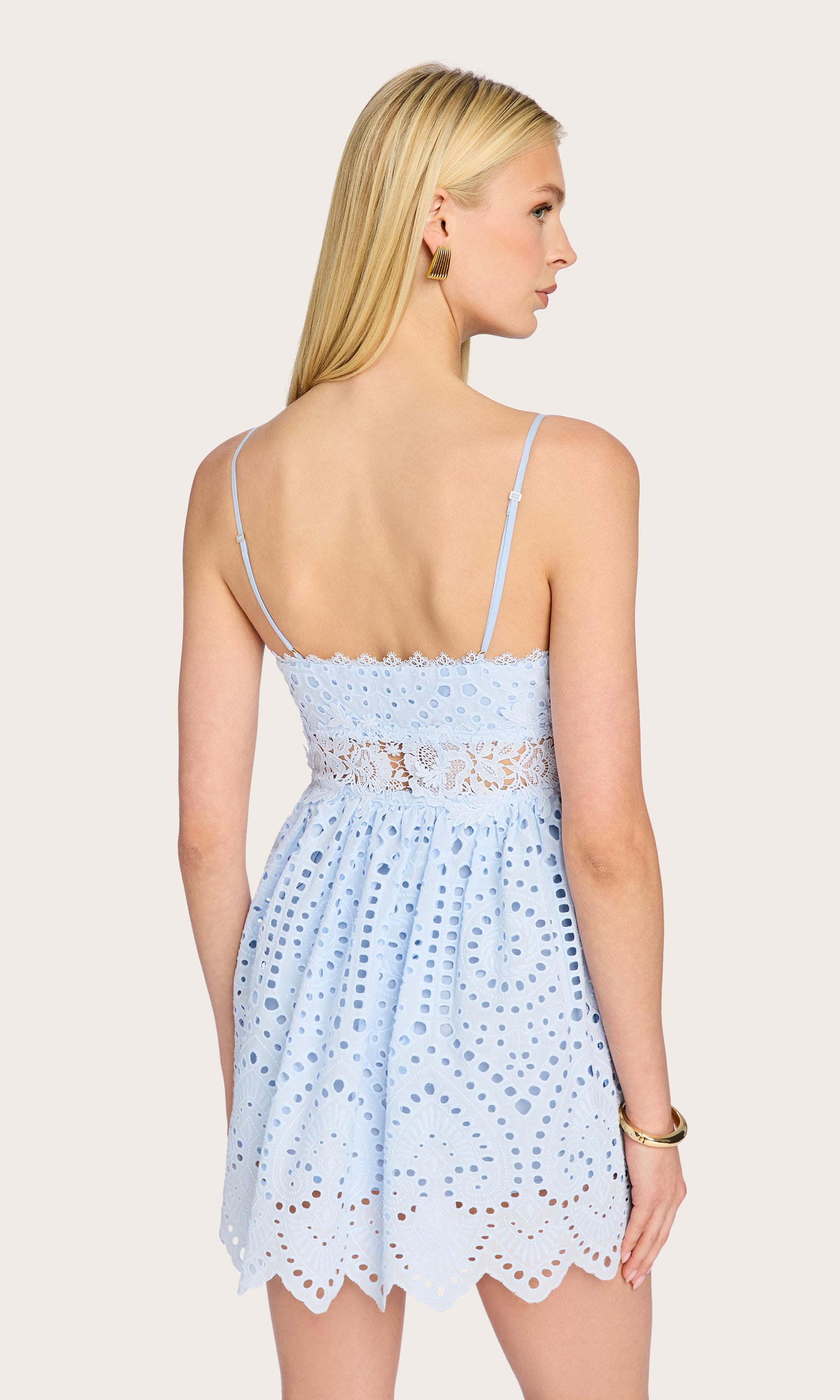 Rear view of the model in the Lilia Cotton Eyelet Mini Dress, drawing attention to the open back and fitted waistband.