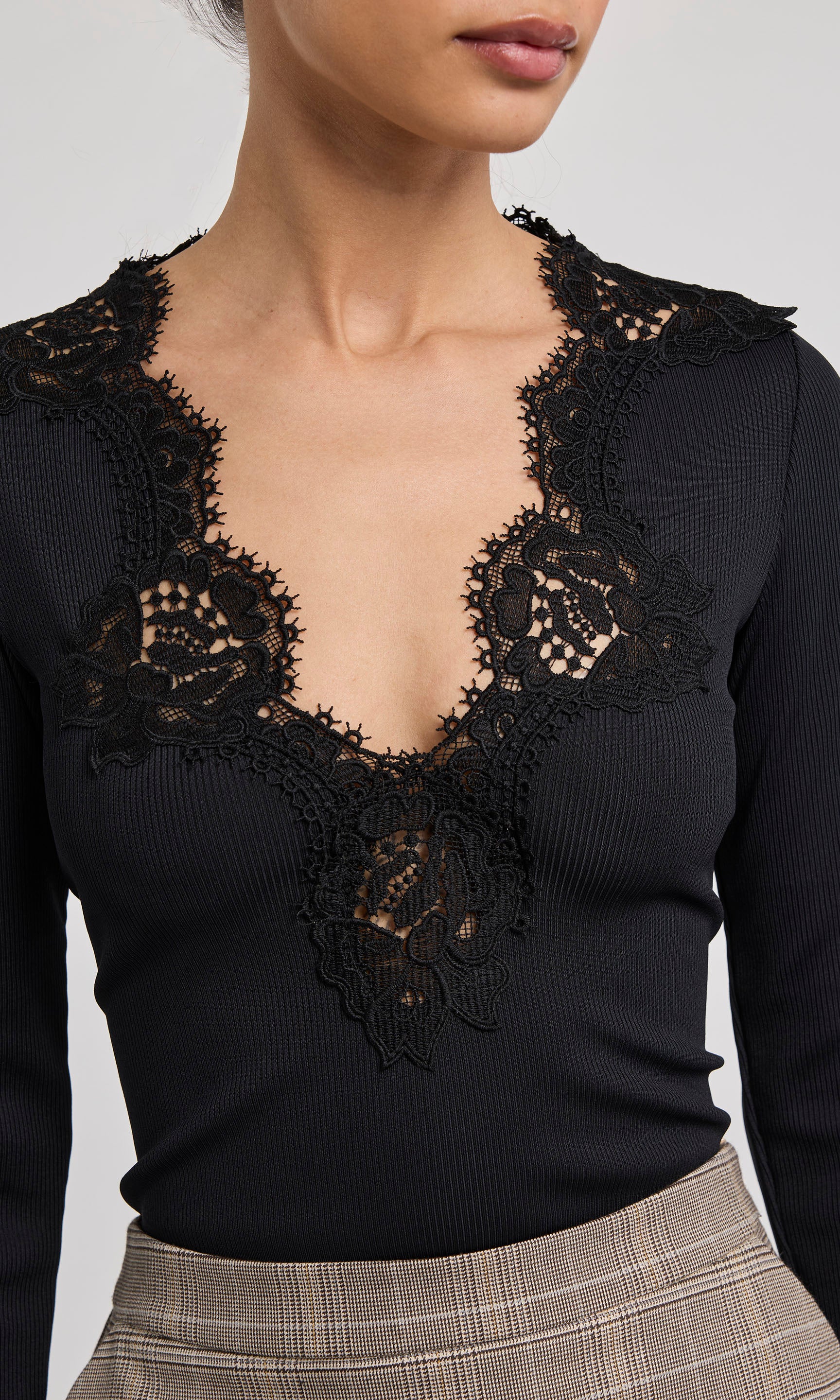 Black lace top worn by a person on a plain background