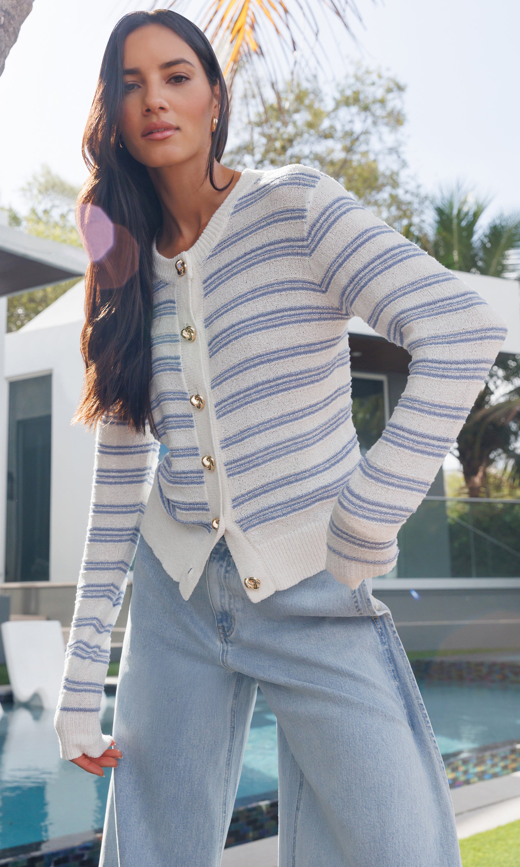 Woman wearing a striped cardigan and jeans by a poolside.