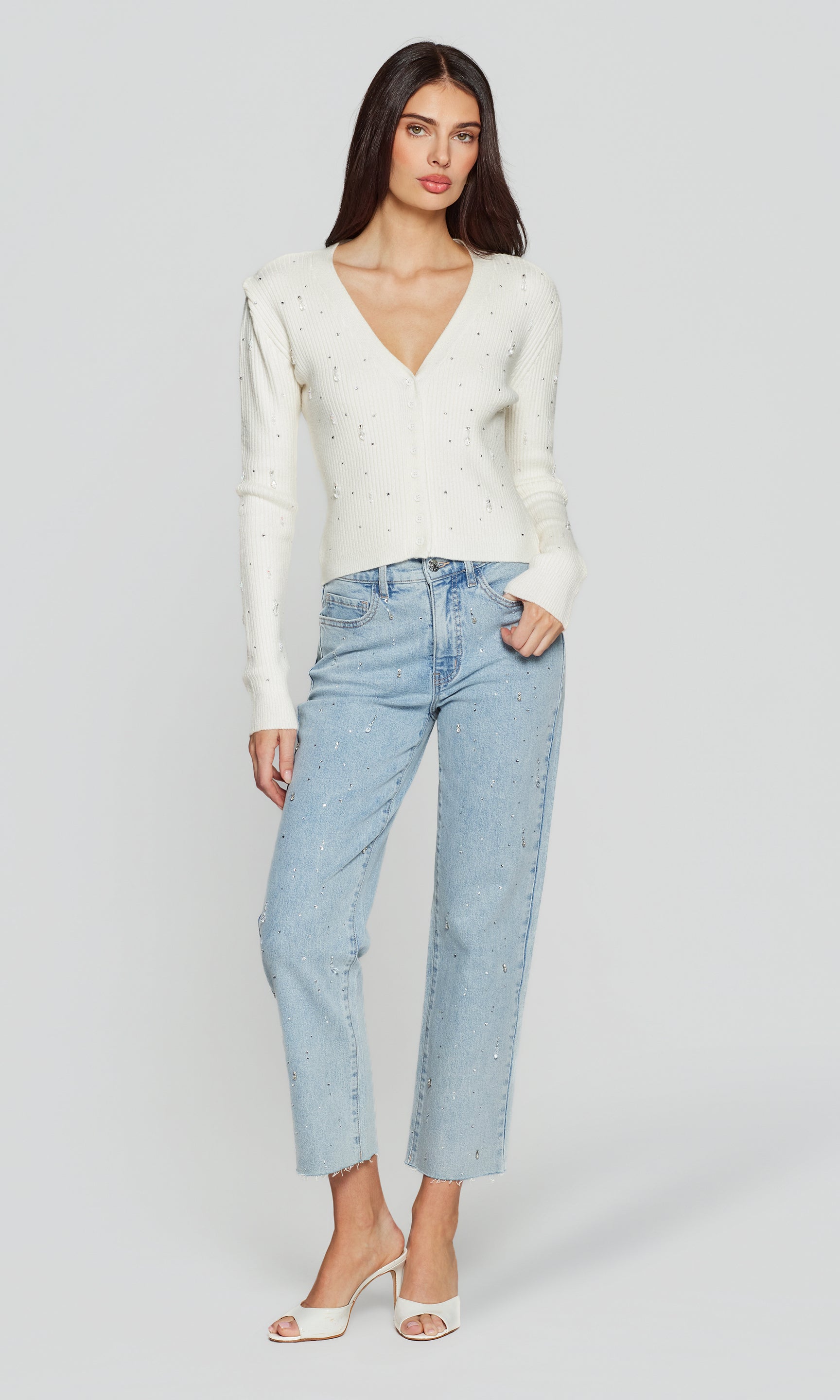 Full body image of woman wearing a white sweater and light blue jeans on a plain background