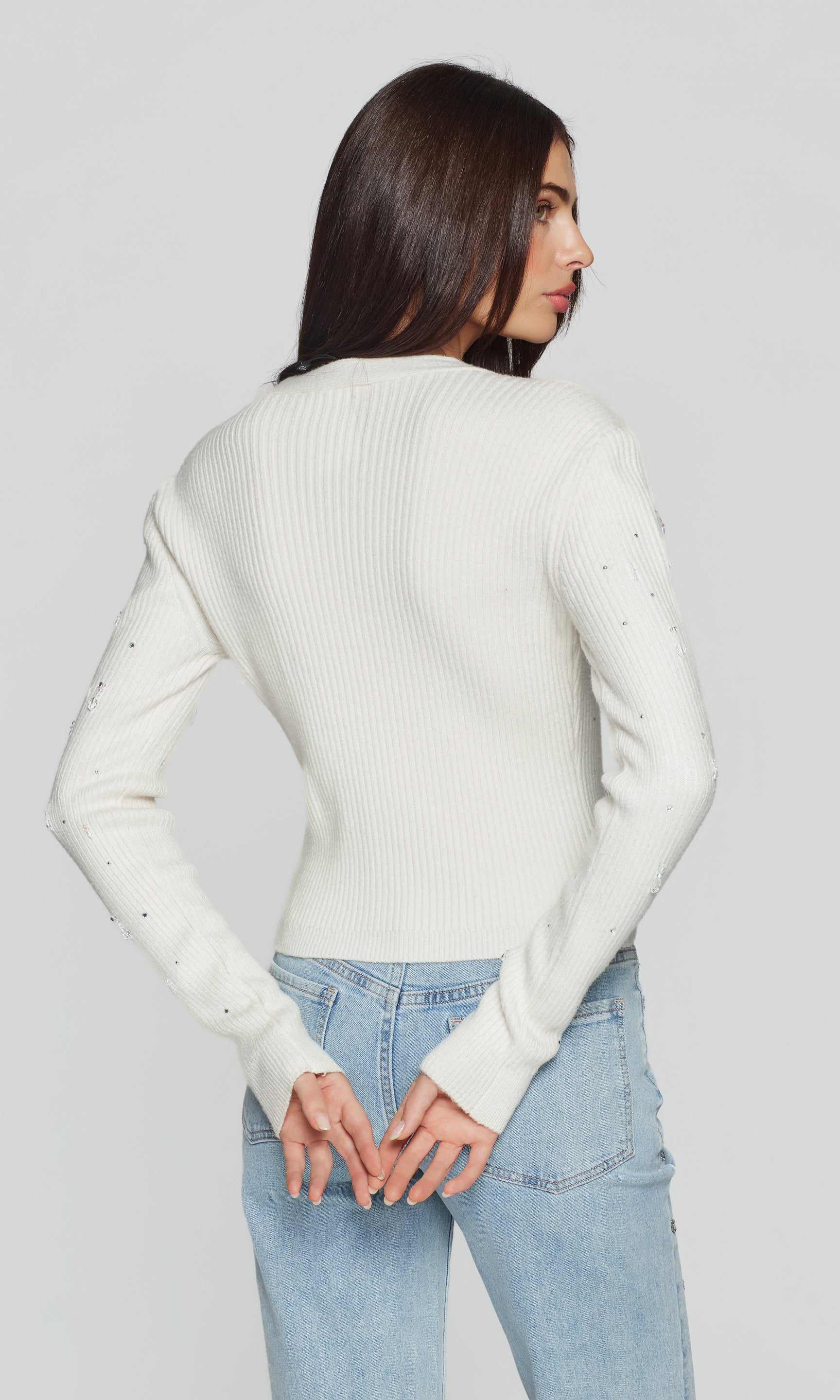 Back view of woman wearing a white sweater and light blue jeans on a plain background