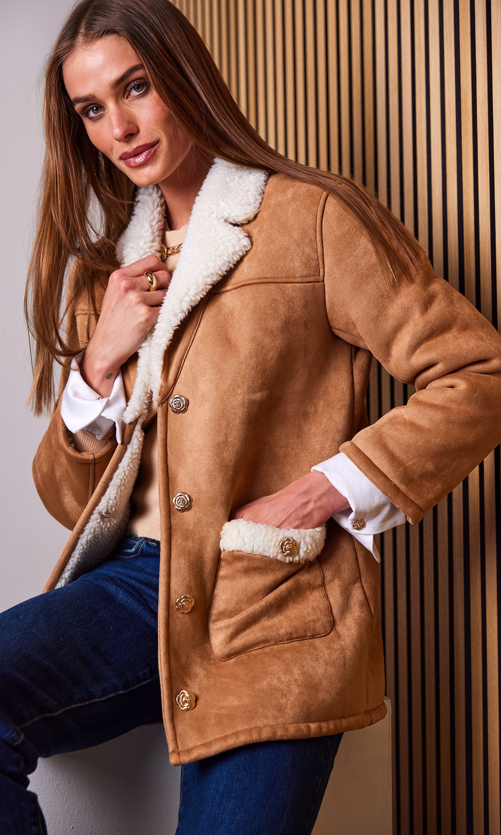 Woman wearing a brown shearling coat with white fur lining against a neutral background