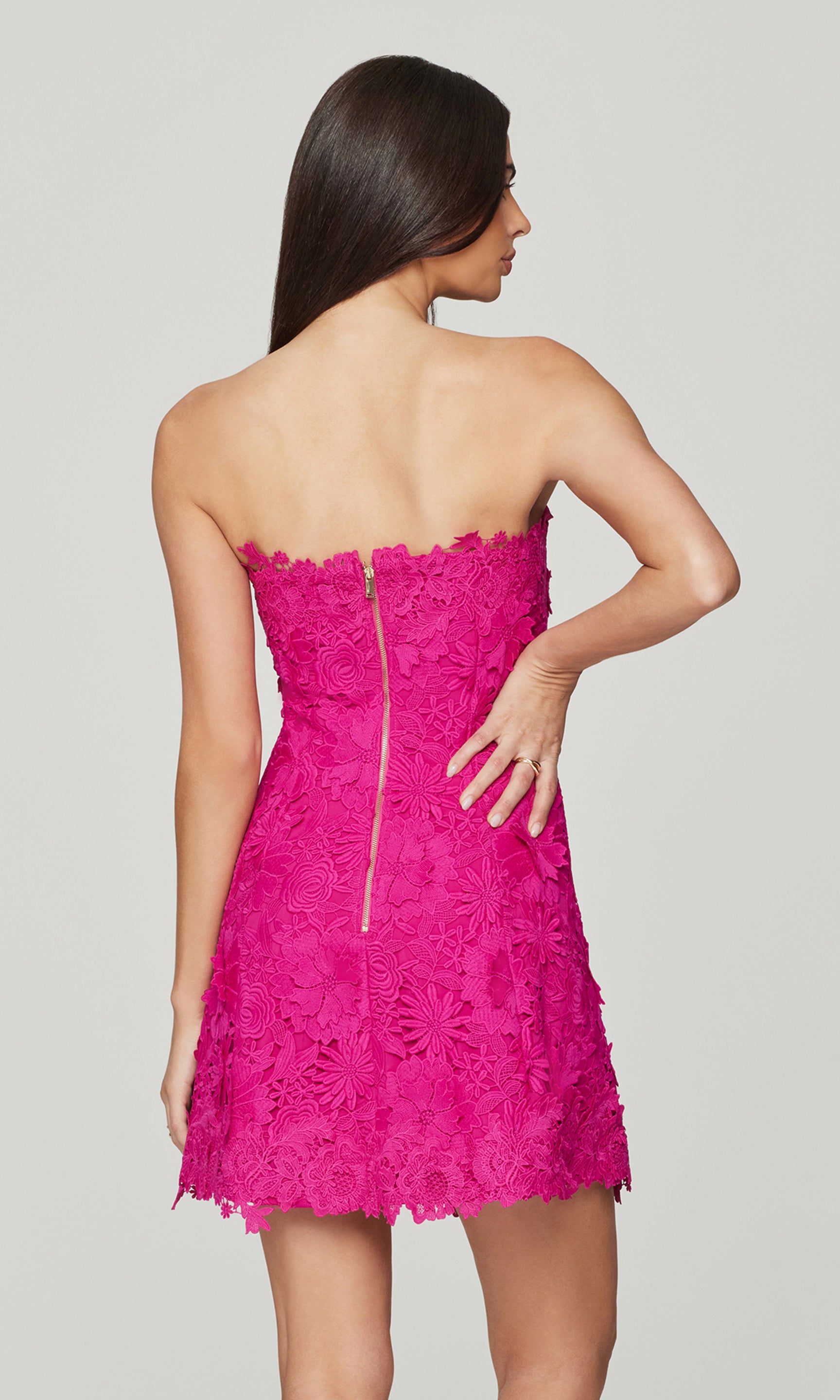 Back view of woman wearing a pink lace dress on a plain background