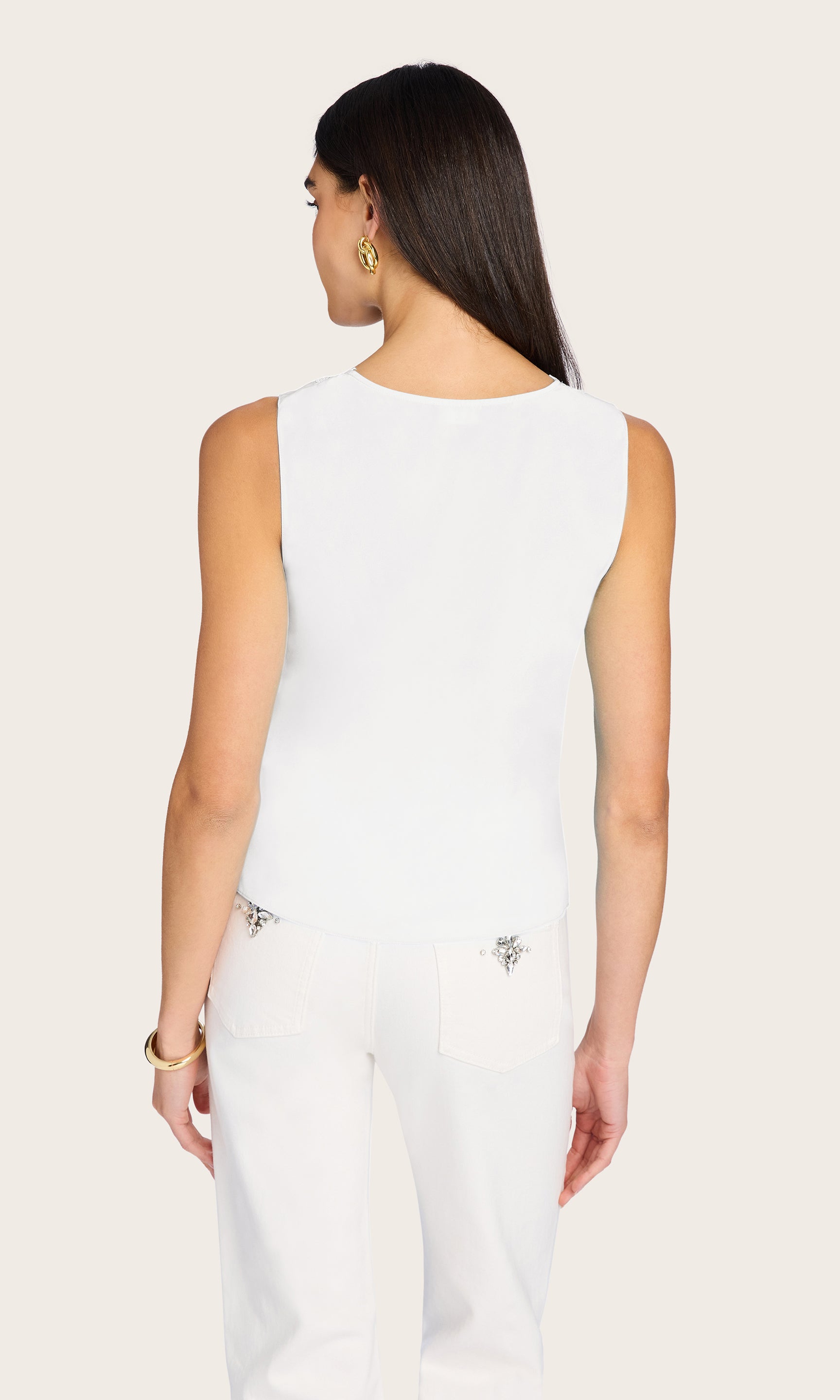 Woman wearing a white sleeveless top and pants on a beige background