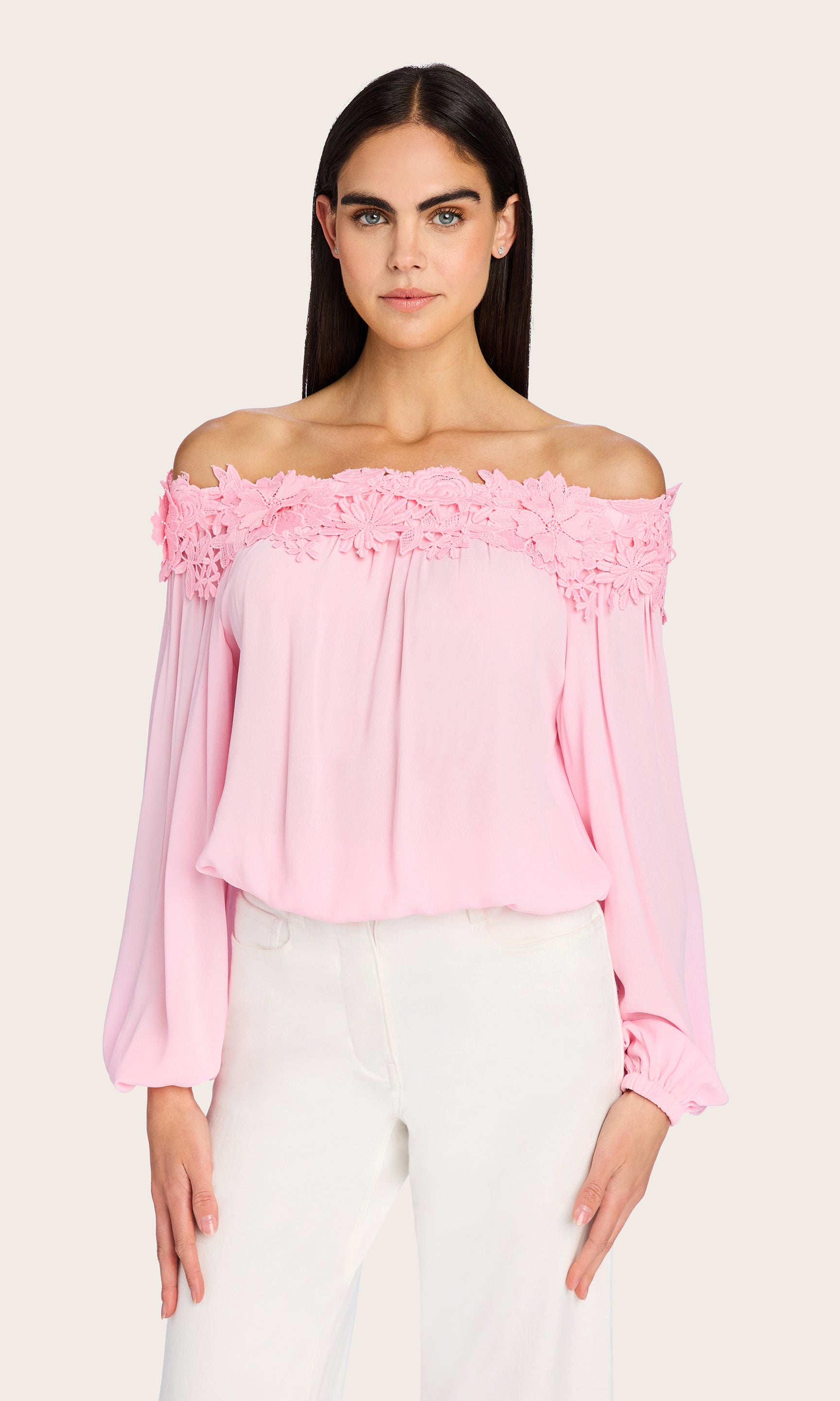 The model wears the Merla Lace Combo Blouse in a front-facing view, styled with white trousers to highlight the blouse’s romantic off-the-shoulder neckline and voluminous sleeves.