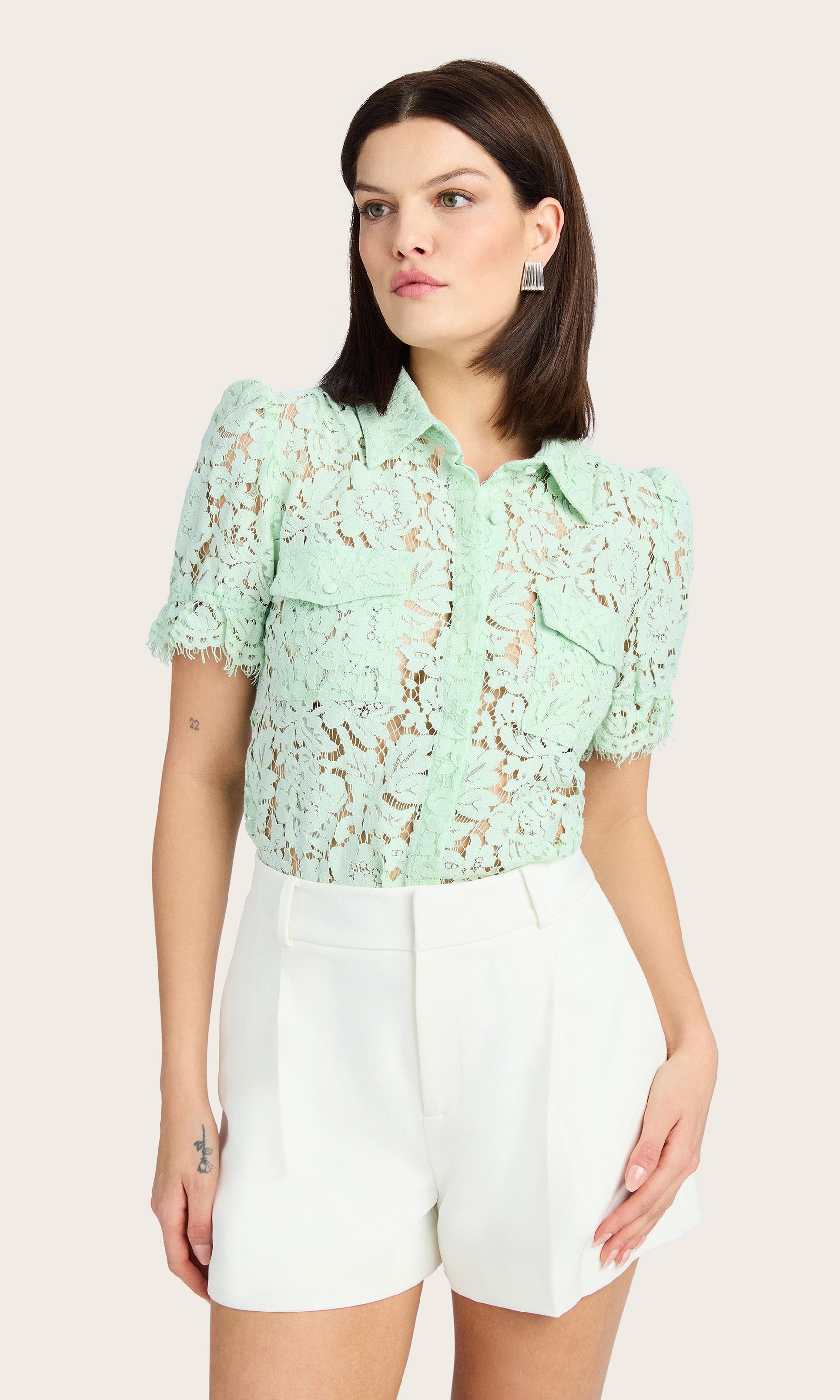 Leaned forward view showcasing the lace detailing and chest flap pockets of the mint green blouse