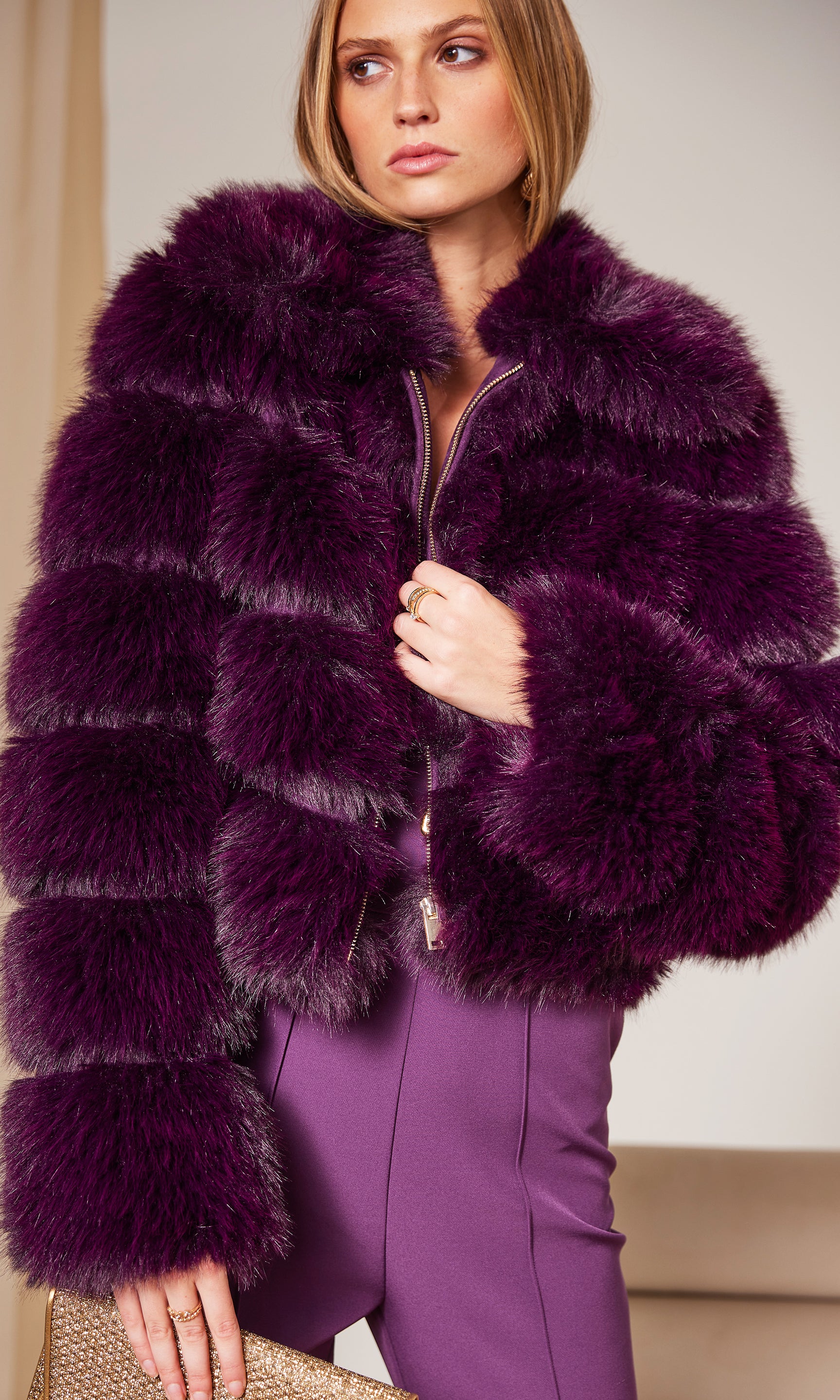 Woman wearing a purple fur coat and pants against a neutral background