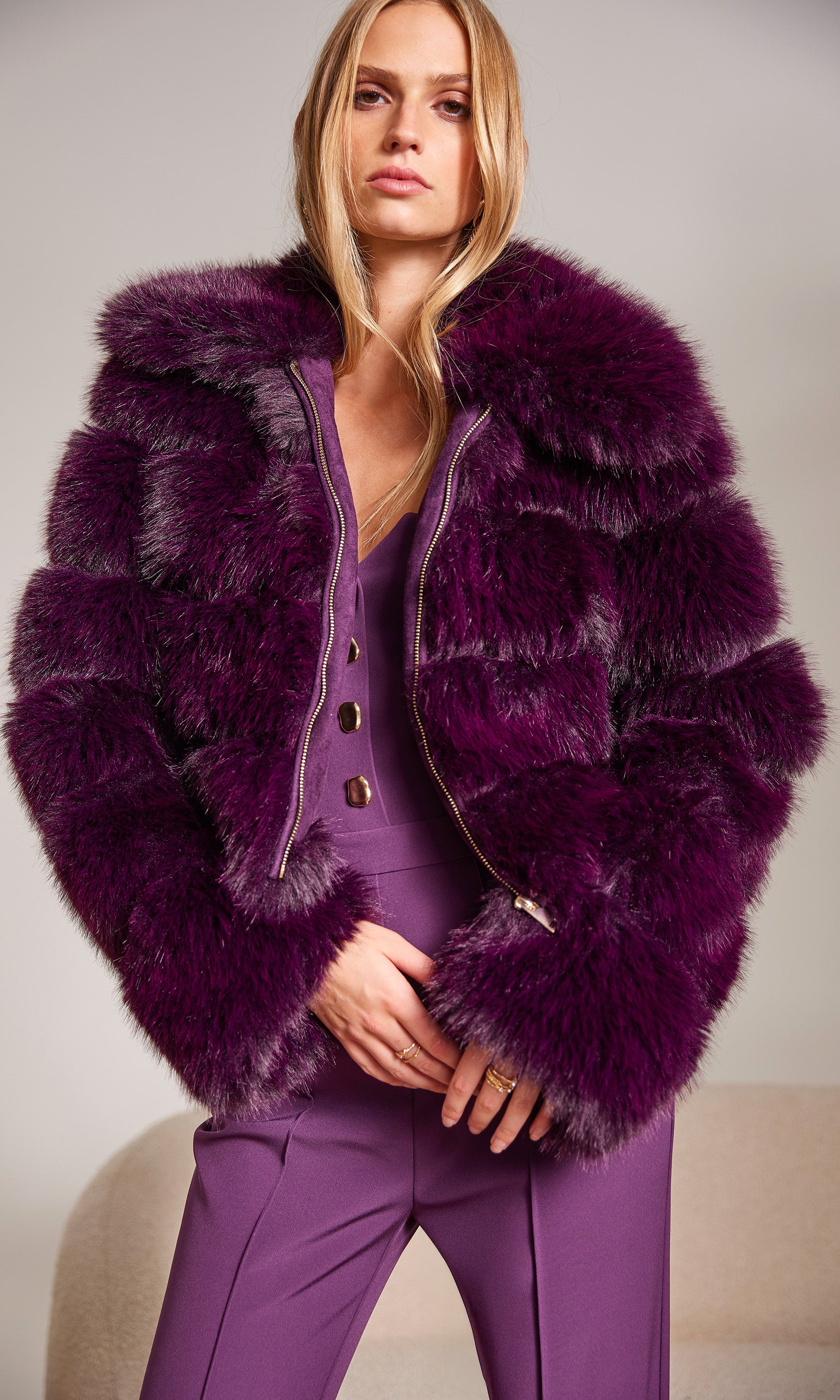 Woman wearing a purple fur coat and matching outfit against a neutral background