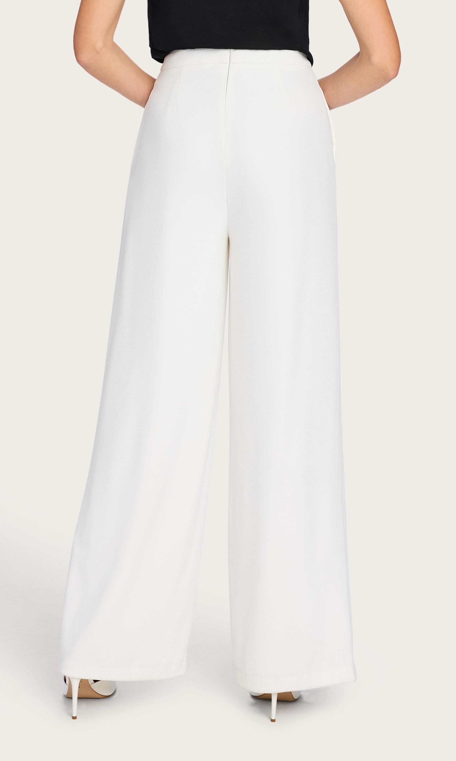 In a rear view, the model highlights the back fit and drape of the Magda Pants, emphasizing the clean waistband and fluid crepe fabric.