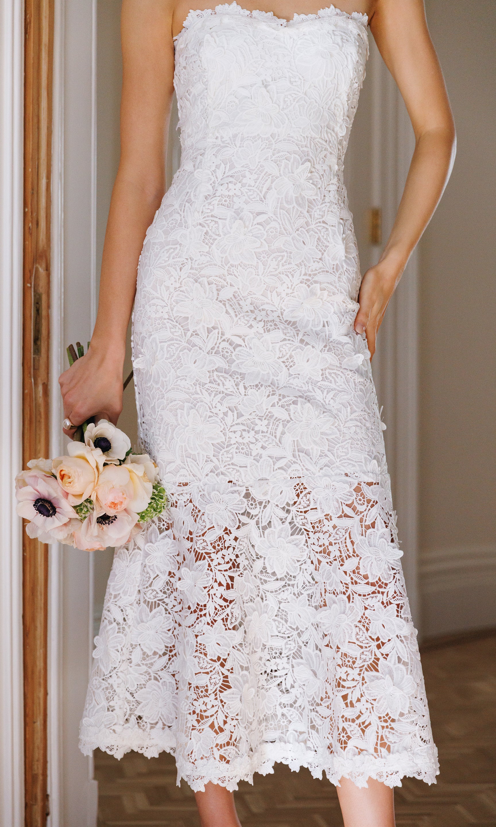 Close-up of white lace dress held by a person with a blurred background