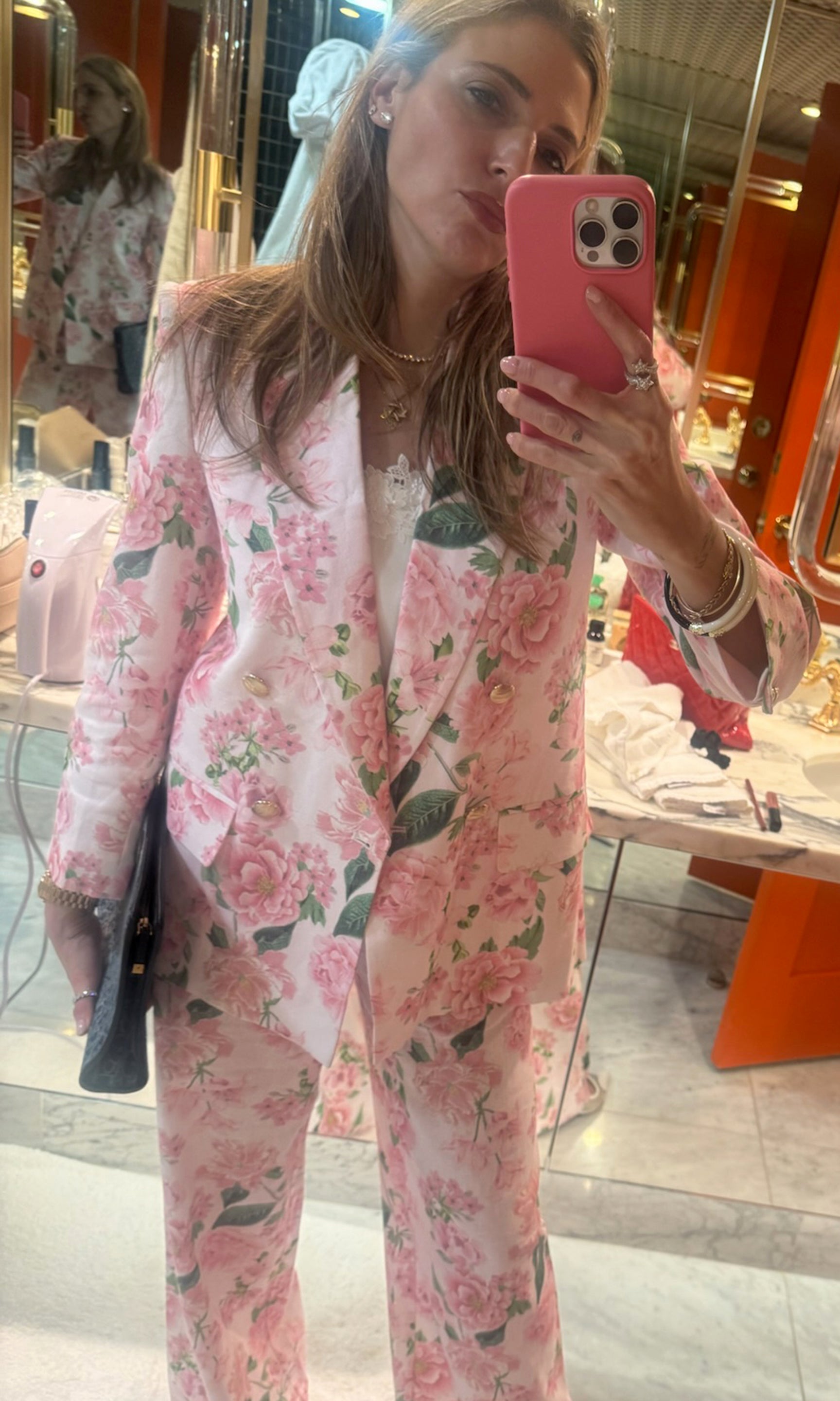 Our founder Roni wearing a pink floral suit taking a mirror selfie.
