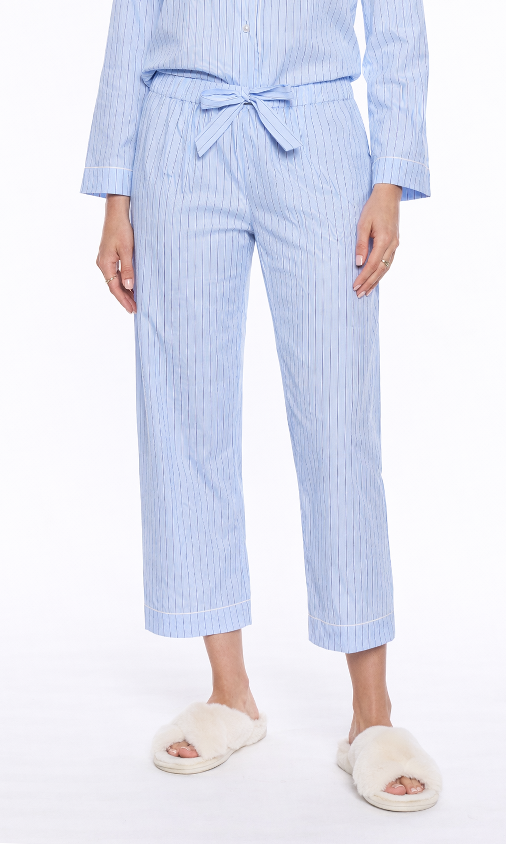 Person wearing a light blue striped pajama pants with white slippers on a white background