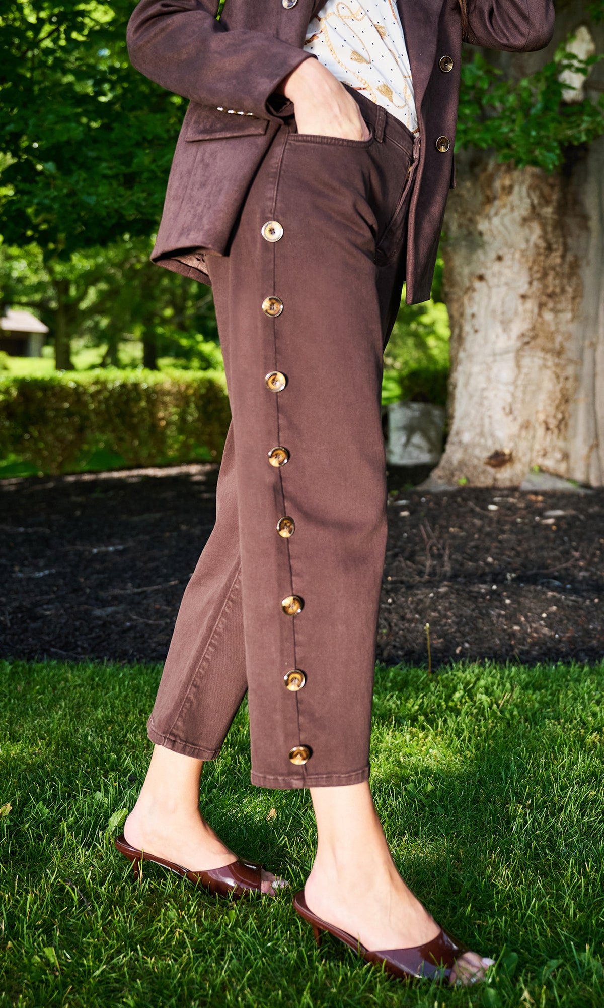 A person outdoors wearing brown cropped pants with large gold-tone decorative buttons down the side, paired with a matching brown blazer.